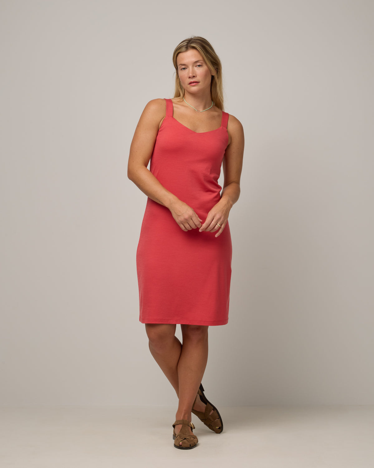 Model wearing Tessa Shelf Bra Dress in Fruit Punch, a vivid red-orange color. Tessa Shelf Bra Dress is a merino wool sleeveless, v-neck, knee length fitted dress available in sizes XS-XXL.