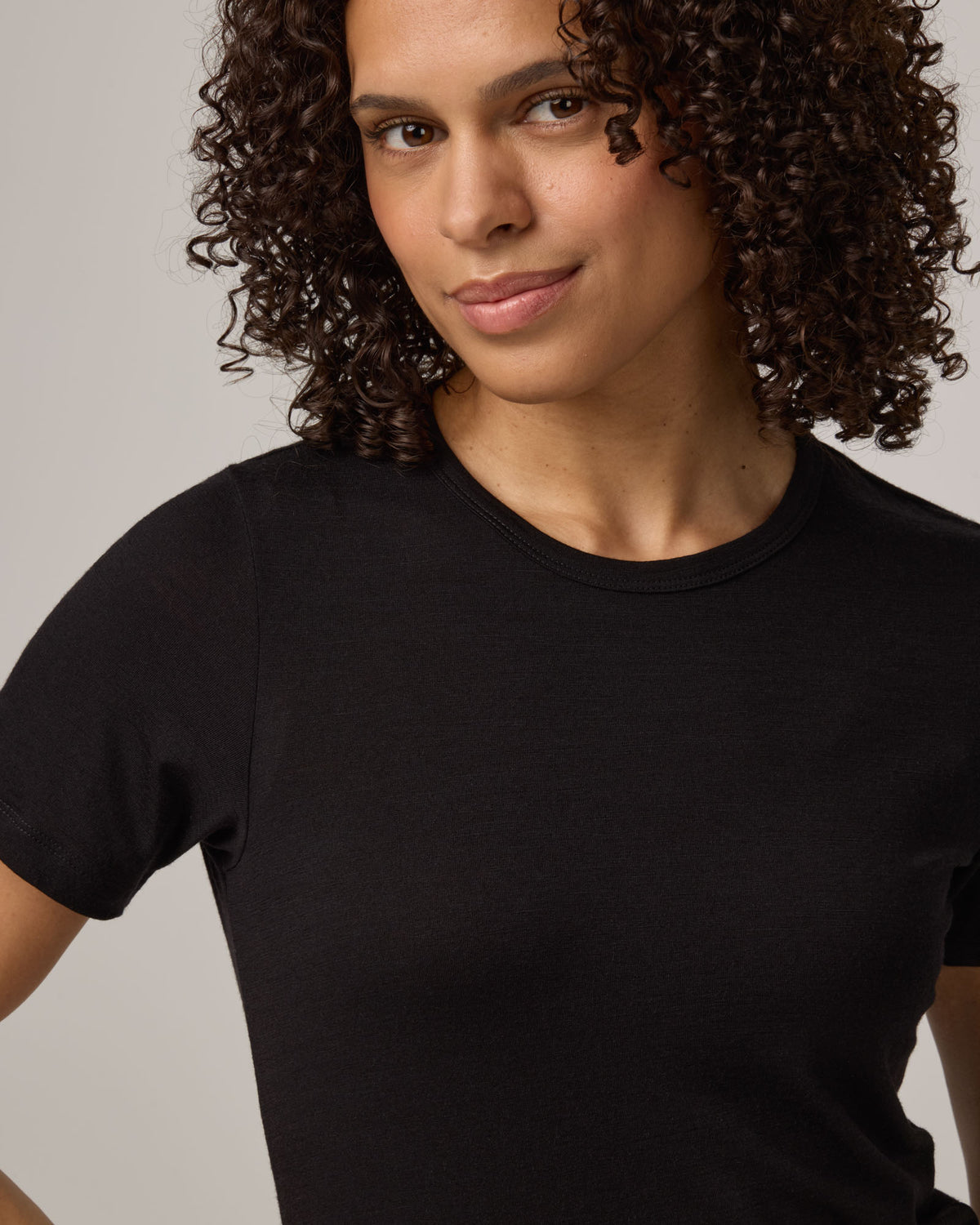 Model wearing Cara 100% Wool Fitted Tee in Black. Cara 100% Wool Fitted Tee is a merino wool short sleeve, crew neck, slim fit tee available in sizes XS-3X.