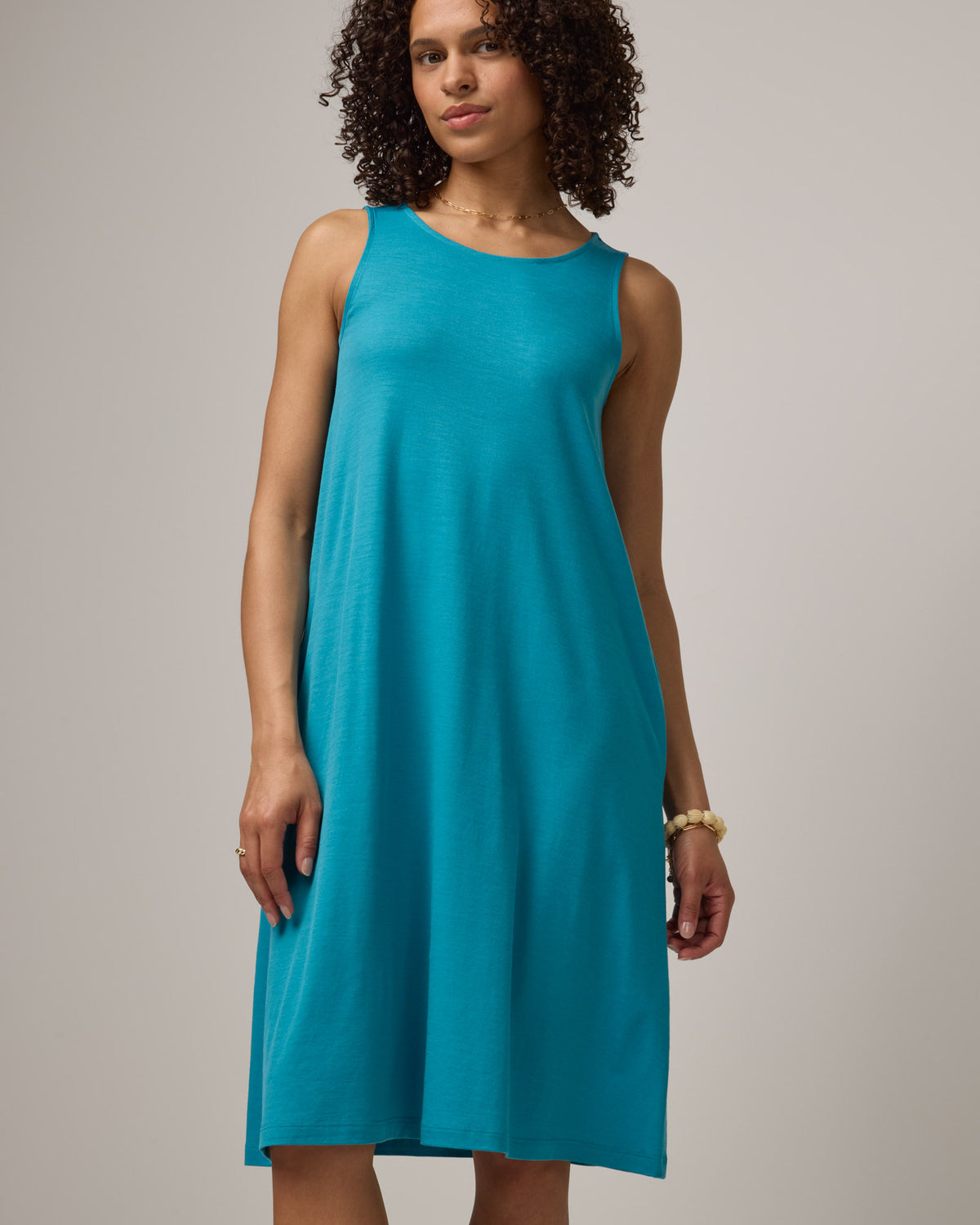 Model wearing Camellia Tank Dress in Sea Blue, a bright sky blue color. Camellia Tank Dress is a merino wool sleeveless, crew neck, knee length swing dress with pockets available in sizes XS-3X Regular, XS-3X Long.