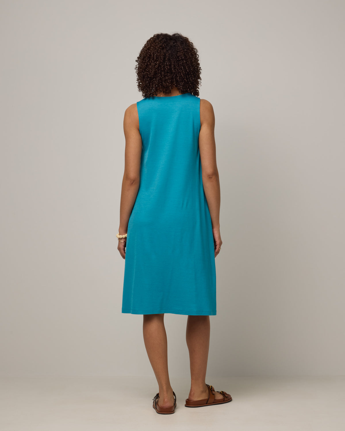 Model wearing Camellia Tank Dress in Sea Blue, a bright sky blue color. Camellia Tank Dress is a merino wool sleeveless, crew neck, knee length swing dress with pockets available in sizes XS-3X Regular, XS-3X Long.