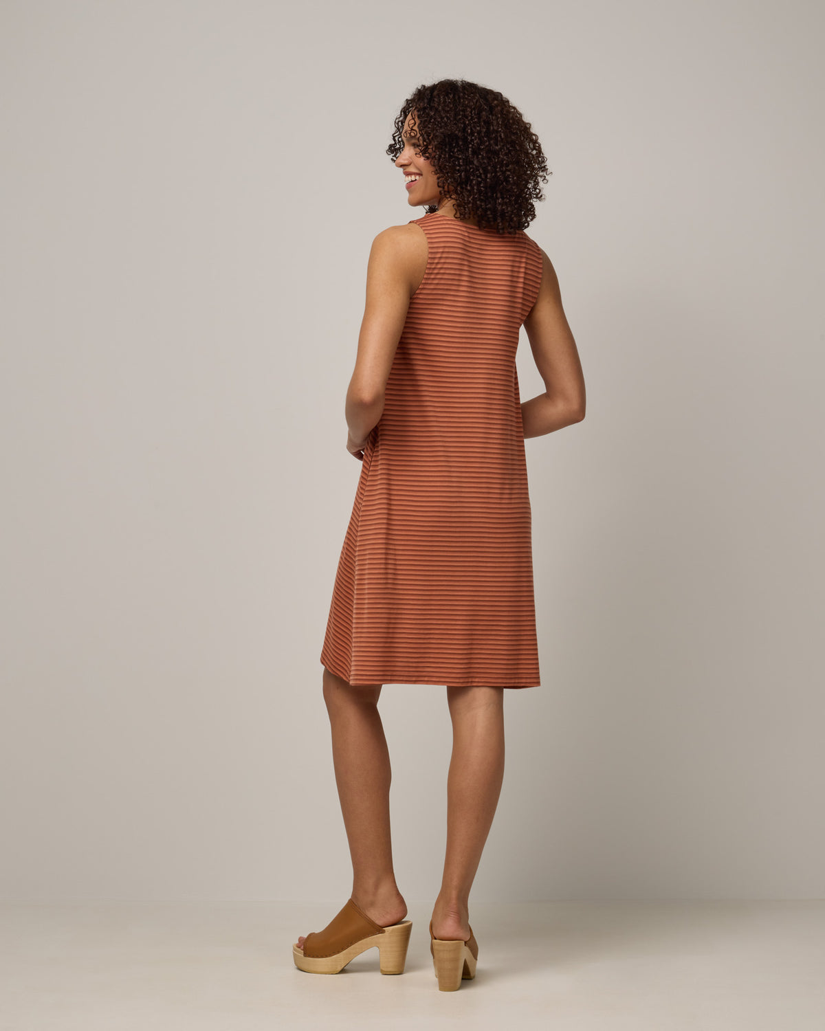 Model wearing Camellia Tank Dress in Cinnamon Tonal Stripe. Camellia Tank Dress is a merino wool sleeveless, crew neck, knee length swing dress with pockets available in sizes XS-3X Regular, XS-3X Long.