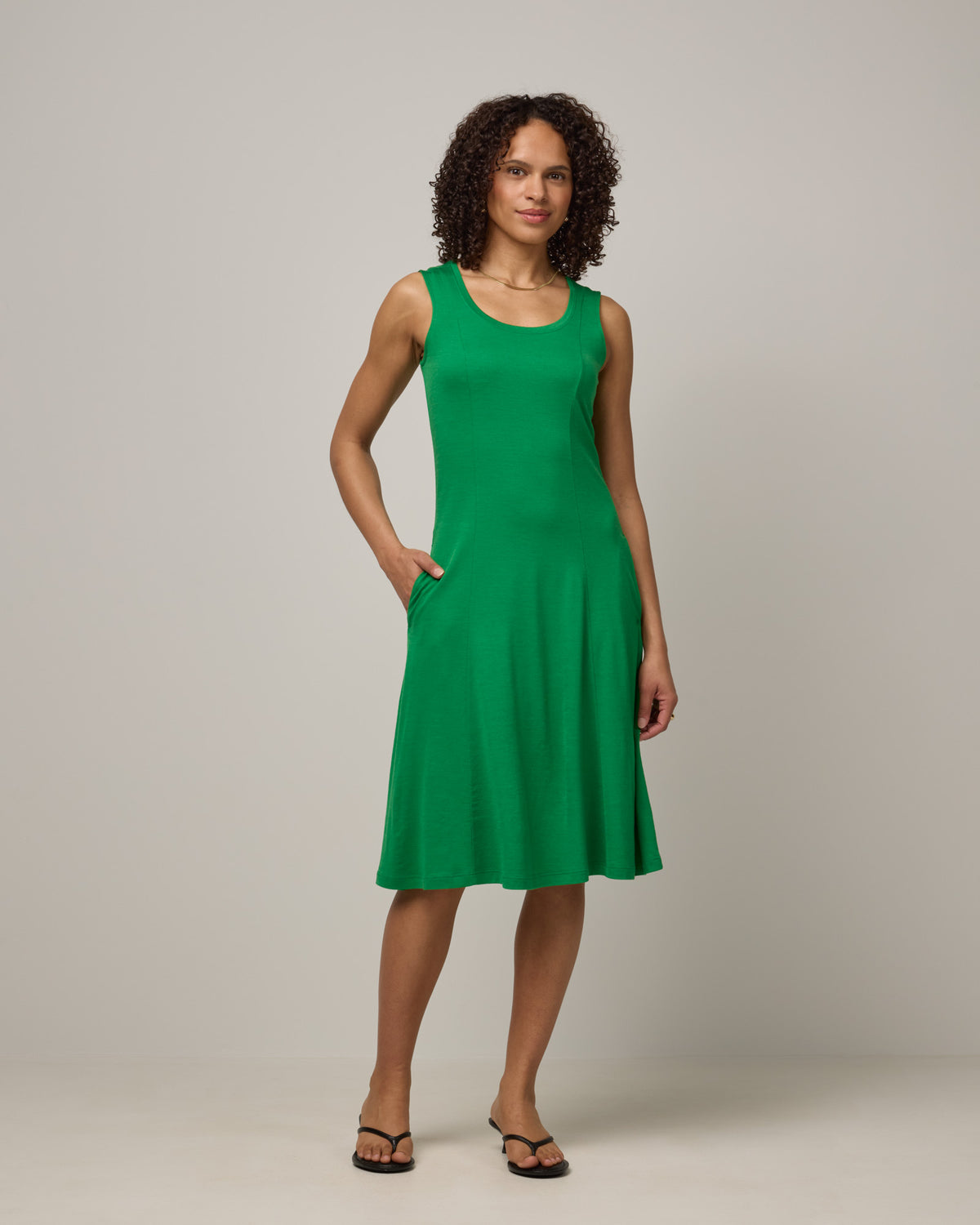 Model wearing Flora Swing Dress in Verde, a bright Kelly green color. Flora Swing Dress is a merino wool sleeveless, scoop neck, knee length swing dress with pockets available in sizes XS-3X.