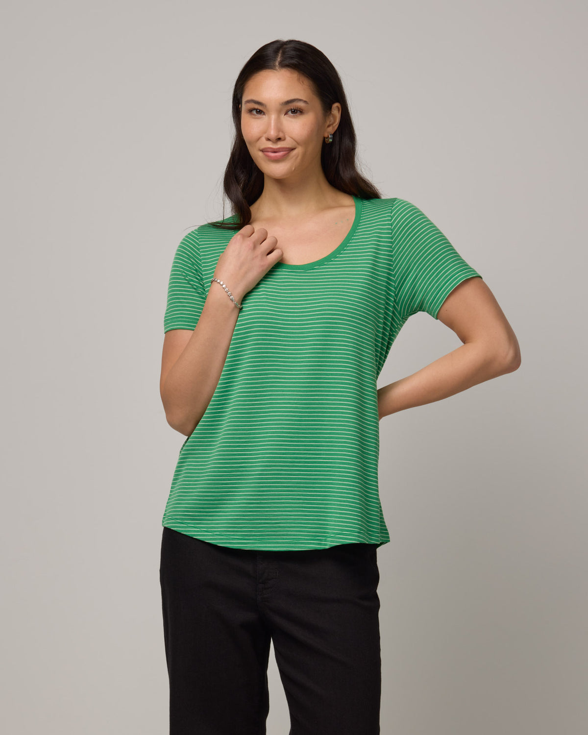 Model wearing Stella Scoop Neck Tee in Verde & Natural White Stripe. Stella Scoop Neck Tee is a merino wool short sleeve, scoop neck t-shirt available in sizes XS-3X.