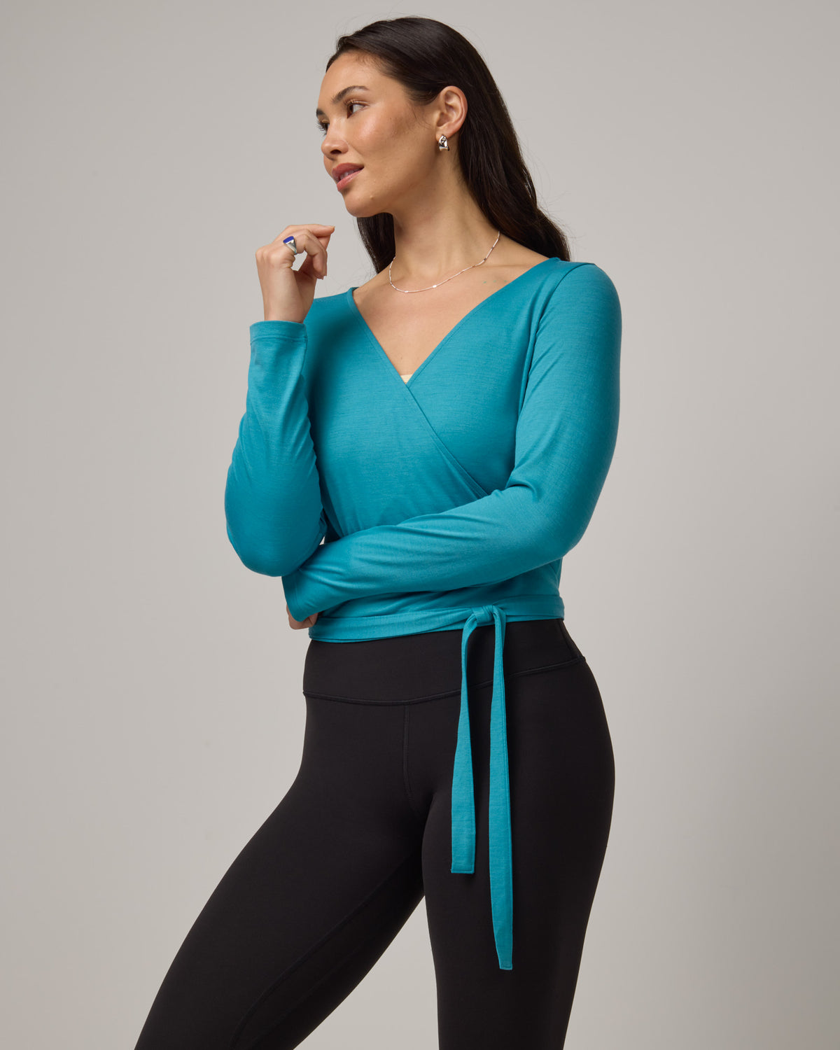 Model wearing Natalia Wrap Top in Sea Blue, a bright sky blue color. Natalia Wrap Top is a merino wool long sleeve, v-neck, slim fit top available in sizes XS-3X.