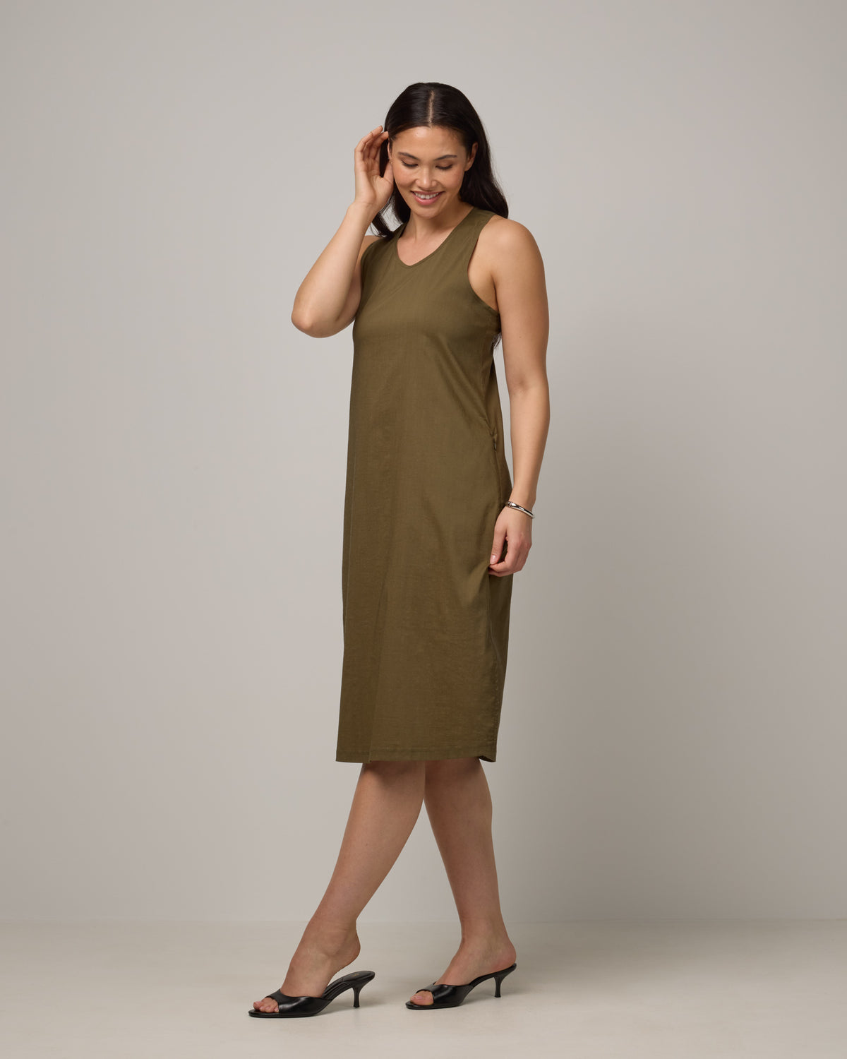 Model wearing Acadia Racerback Dress in Olive. Acadia Racerback Dress is a merino wool sleeveless, v-neck, midi length fitted dress available in sizes XS-XXL.