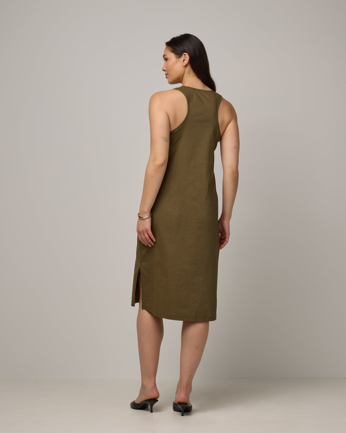 Model wearing Acadia Racerback Dress in Olive. Acadia Racerback Dress is a merino wool sleeveless, v-neck, midi length fitted dress available in sizes XS-XXL.