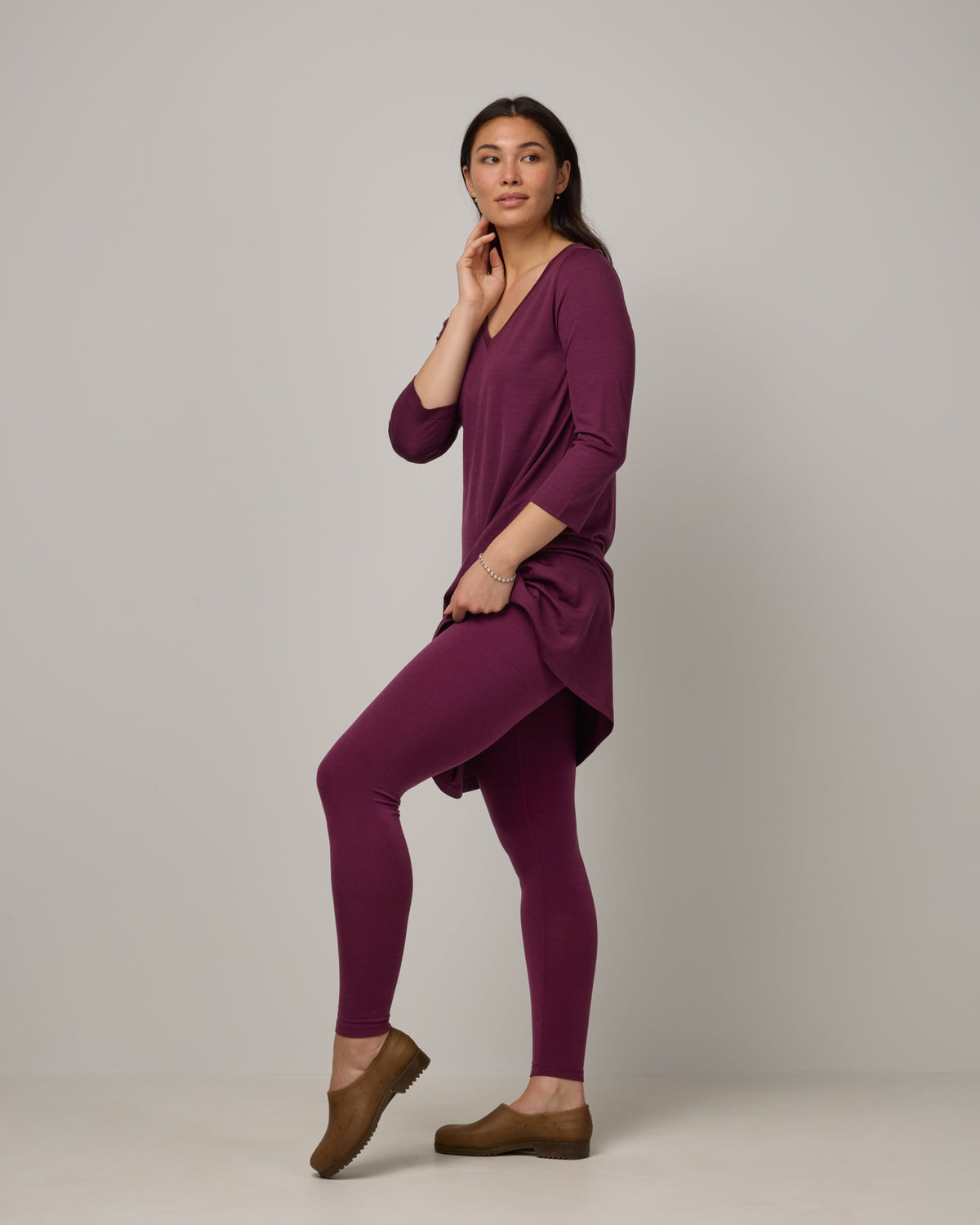 Model wearing Roam Legging in Plum, a reddish-purple color. Roam Legging is a lightweight merino wool legging with pockets available in sizes XS-3X.