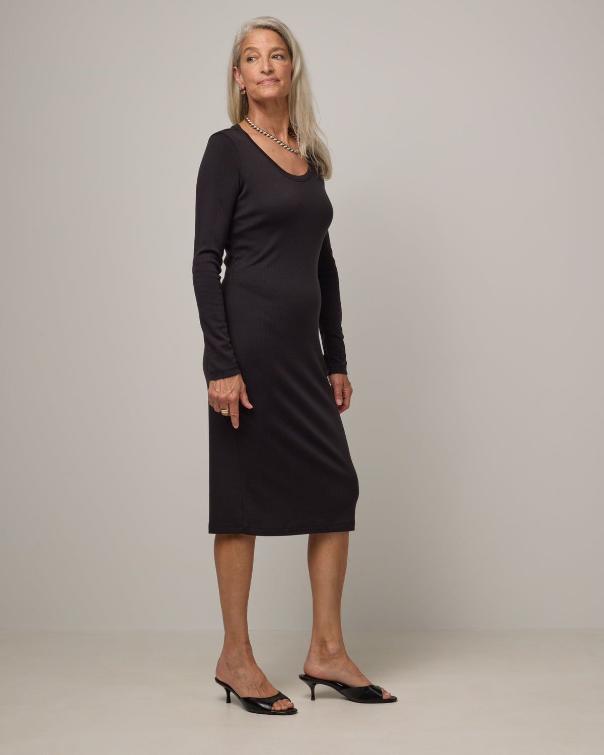 Model wearing Lex Ribbed Dress in Black. Lex Ribbed Dress is a merino wool long sleeve, scoop neck, fitted midi dress available in sizes XS-XXL Regular & XS-XL Petite.
