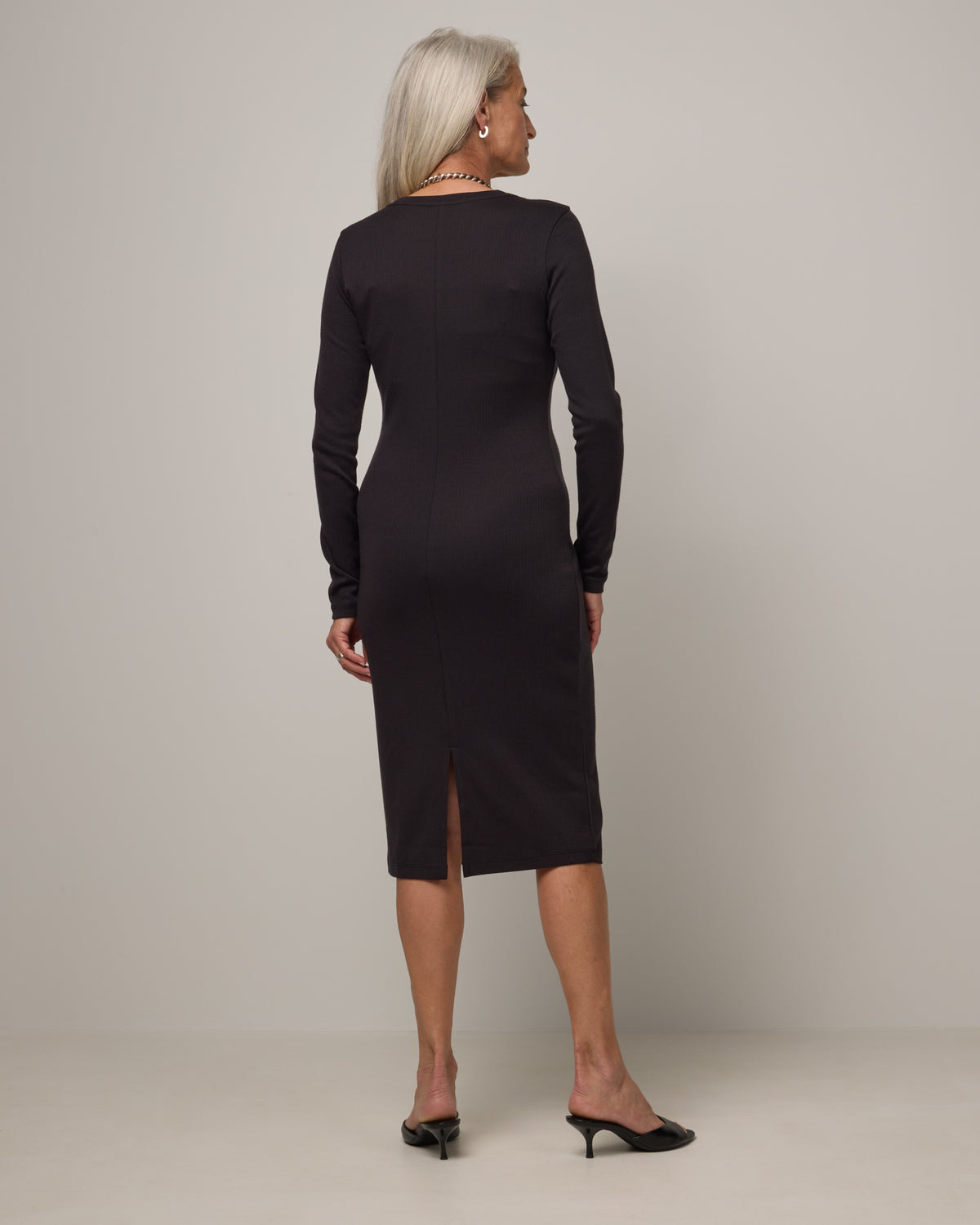 Model wearing Lex Ribbed Dress in Black. Lex Ribbed Dress is a merino wool long sleeve, scoop neck, fitted midi dress available in sizes XS-XXL Regular & XS-XL Petite.