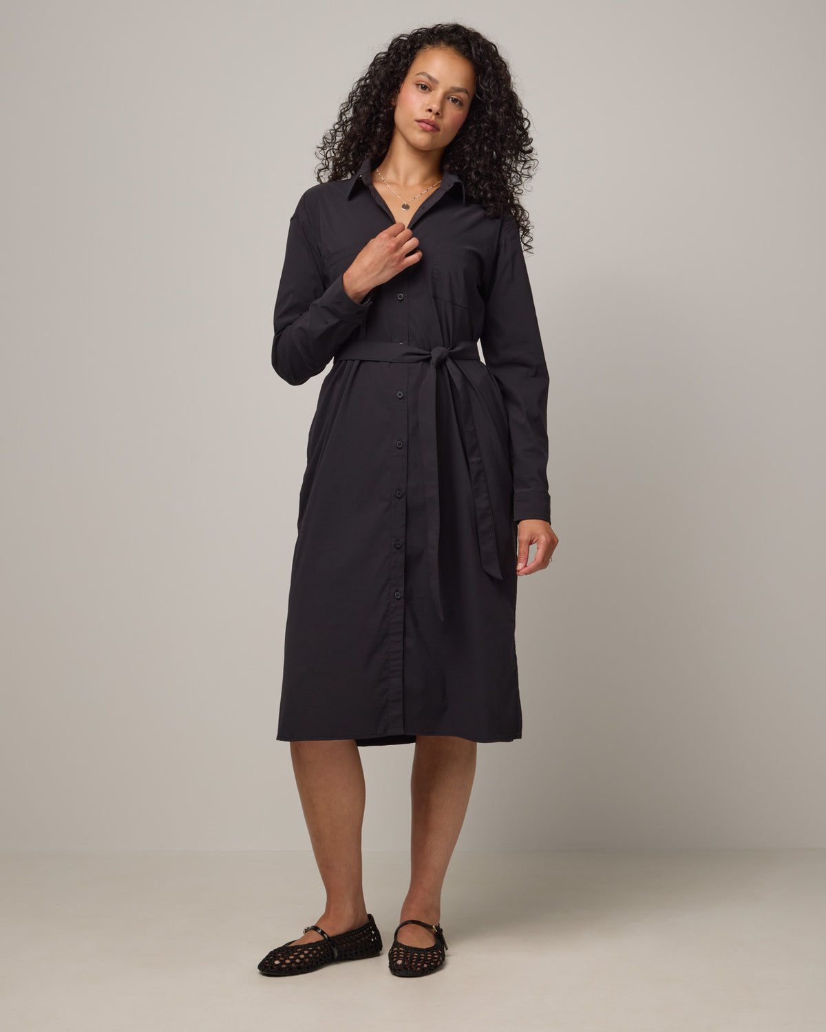 Model wearing Victoria Shirt Dress in Black. Victoria Shirt Dress is a merino wool long sleeve, midi length, button-front dress with pockets and removable belt available in sizes XS-XXL.