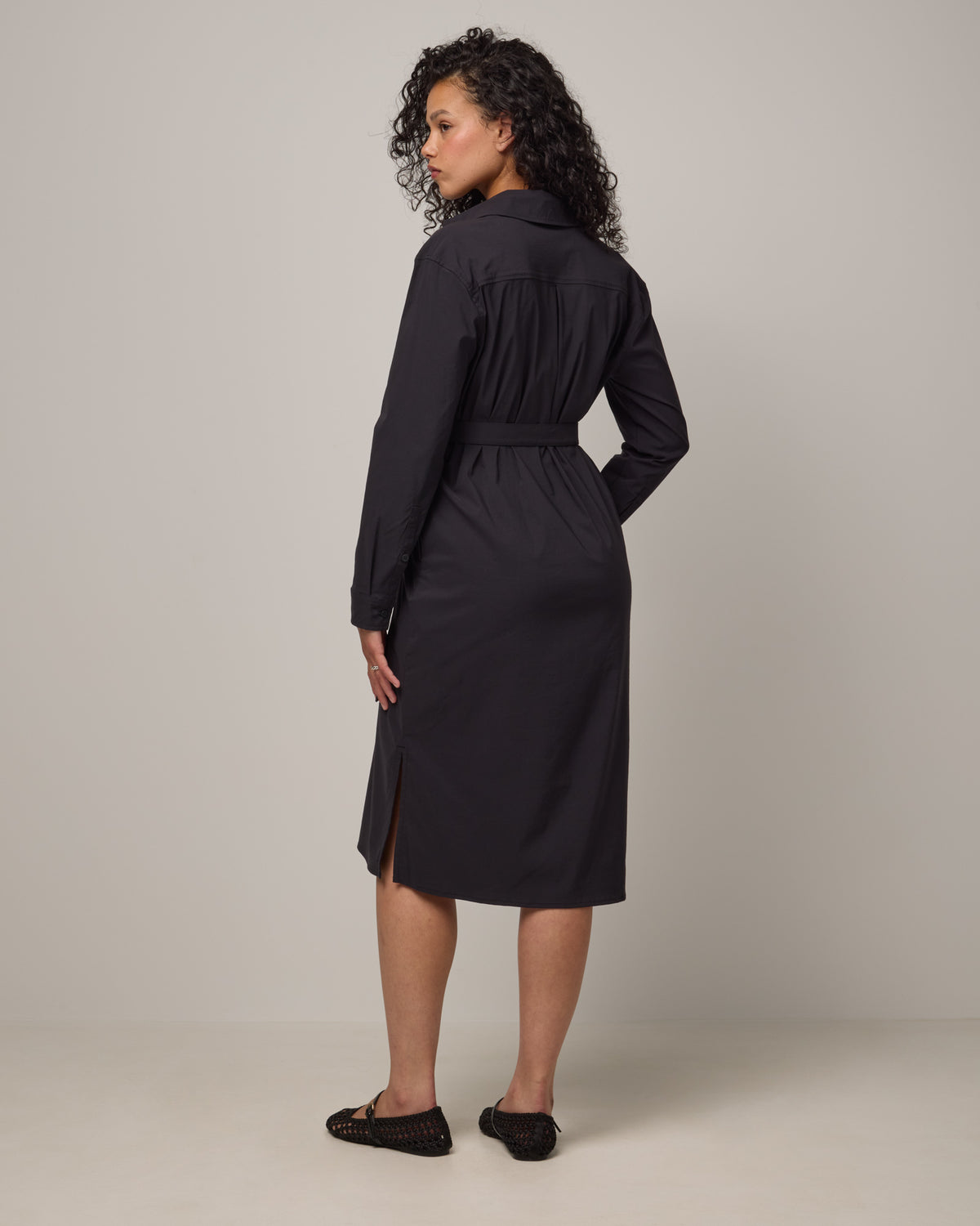 Model wearing Victoria Shirt Dress in Black. Victoria Shirt Dress is a merino wool long sleeve, midi length, button-front dress with pockets and removable belt available in sizes XS-XXL.