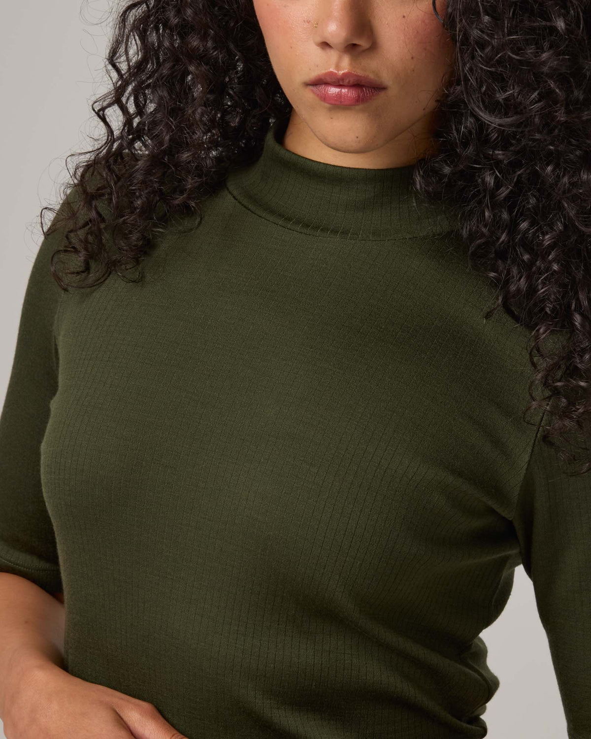 Model wearing Krystal Mock Neck Top in Forest Night, a dark forest green color. Krystal Mock Neck Top is a merino wool half-sleeve, mock-neck ribbed tee available in sizes XS-XXL.