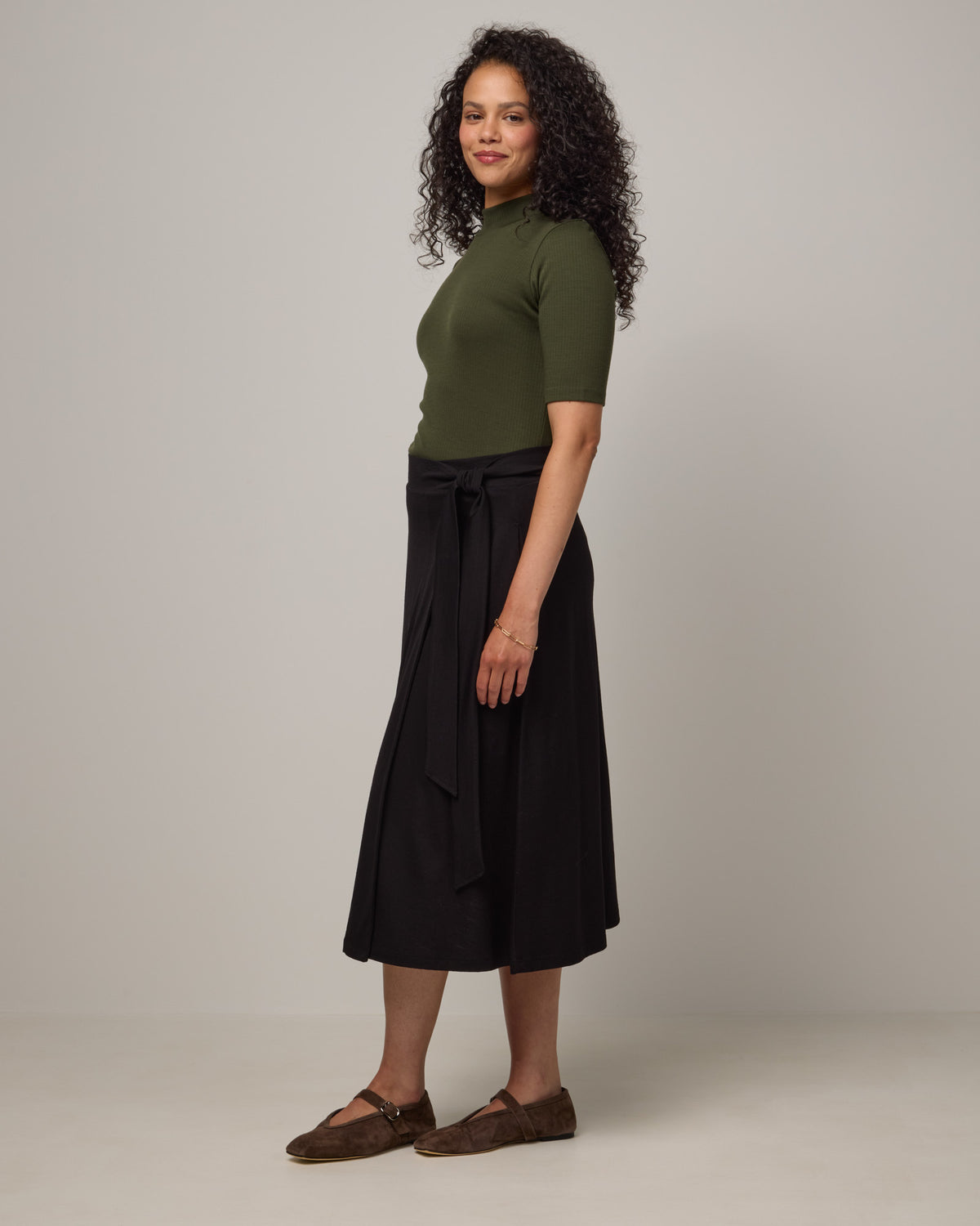 Model wearing Krystal Mock Neck Top in Forest Night, a dark forest green color. Krystal Mock Neck Top is a merino wool half-sleeve, mock-neck ribbed tee available in sizes XS-XXL.