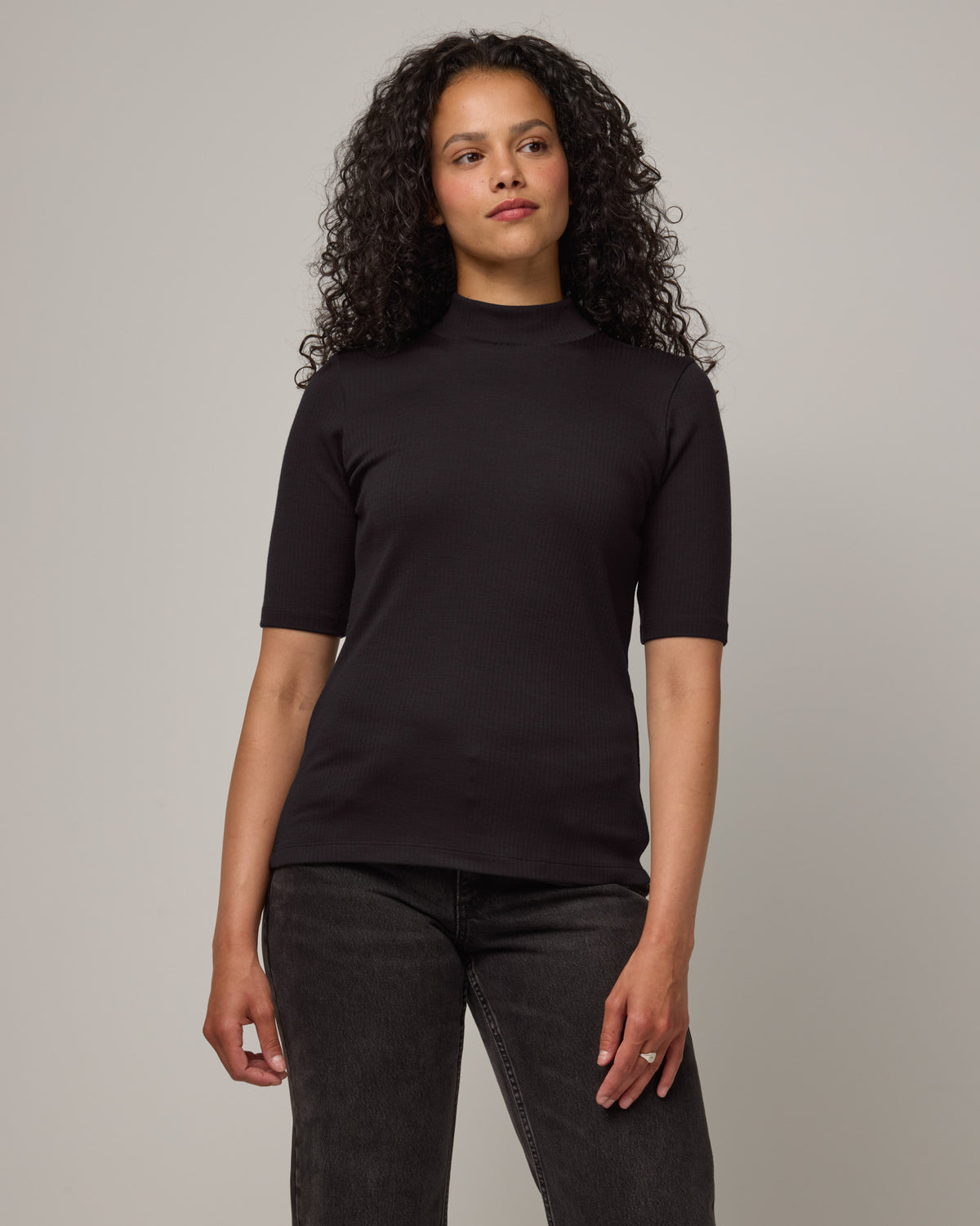 Model wearing Krystal Mock Neck Top in Black. Krystal Mock Neck Top is a merino wool half-sleeve, mock-neck ribbed tee available in sizes XS-XXL.