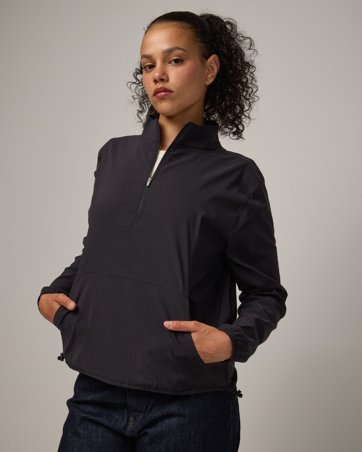 Model wearing Venus Quarter Zip in Black. Venus Quarter Zip is a merino wool lightweight long sleeve pullover with a front pocket available in sizes XS-XXL. 