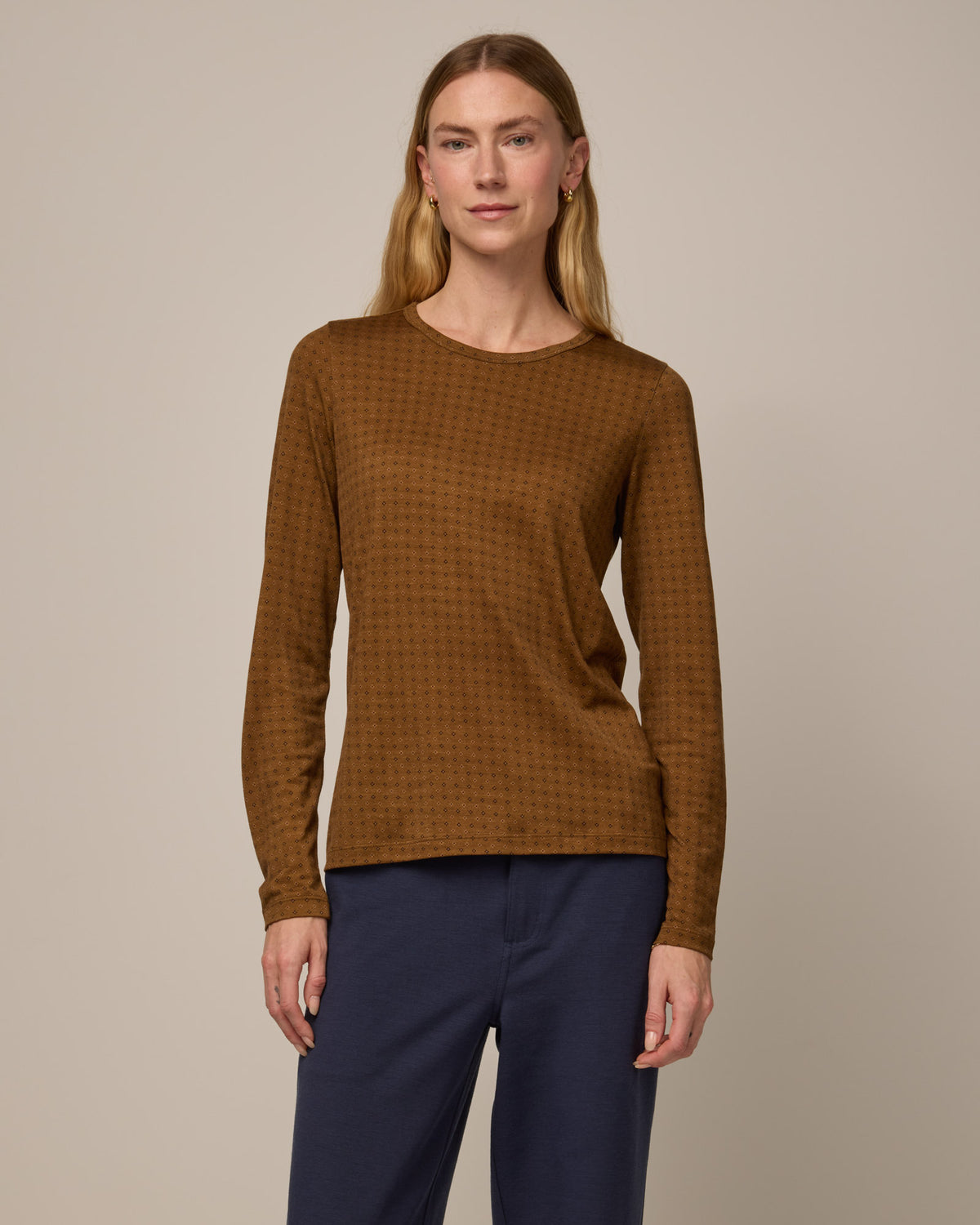 Model wearing Sloan Signature Fitted Tee in Geo Stamp Print, a dainty, neutral, geometric print on a dark ochre background. Sloan Signature Fitted Tee is a merino wool long sleeve, crew neck, slim fit tee available in sizes XS-3X.