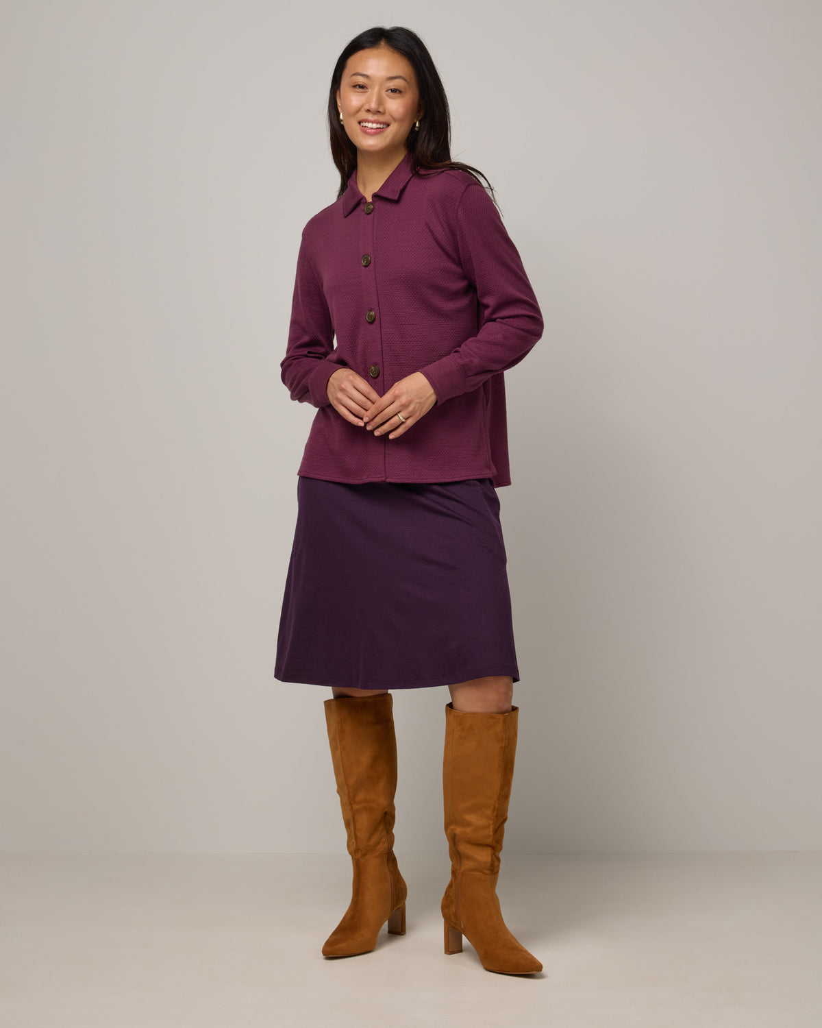 Model wearing Helena Skirt in Cassis, a deep purple color. Helena Skirt is a merino wool knee length skirt with pockets available in sizes XS-3X.