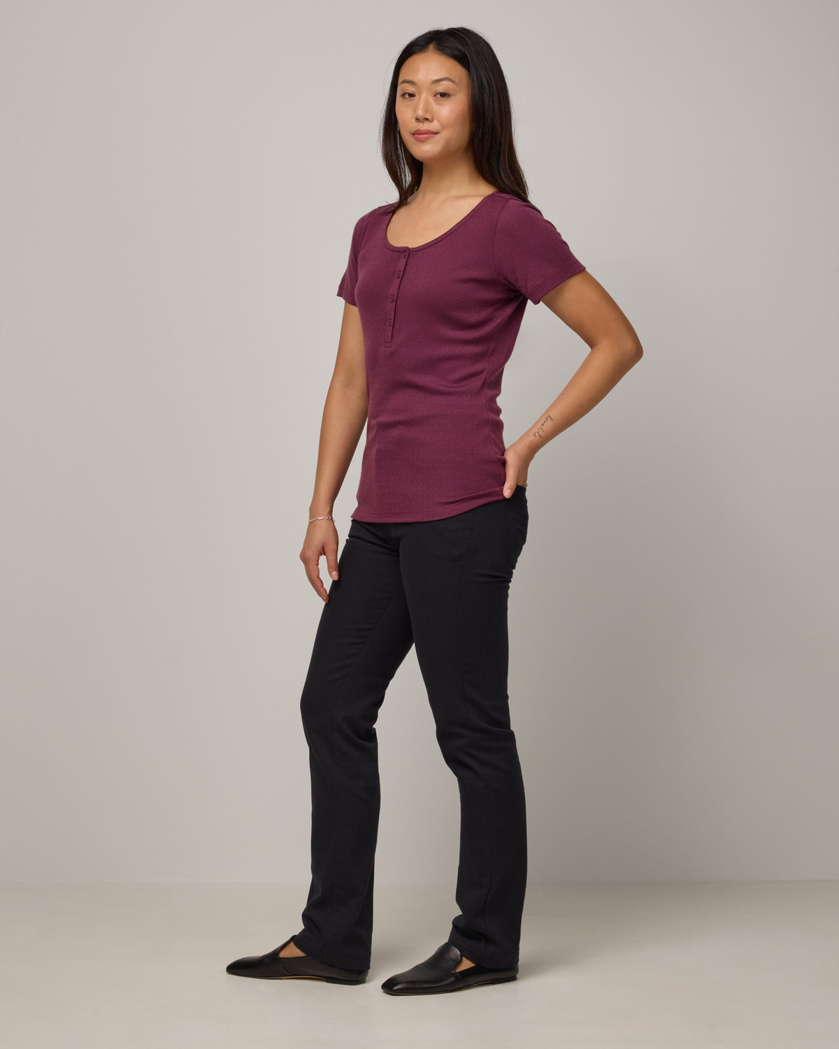 Model wearing Marie Pointelle Henley in Plum, a reddish purple color. Marie Pointelle Henley is a short sleeve, scoop neck, fitted top available in sizes XS-3X. 