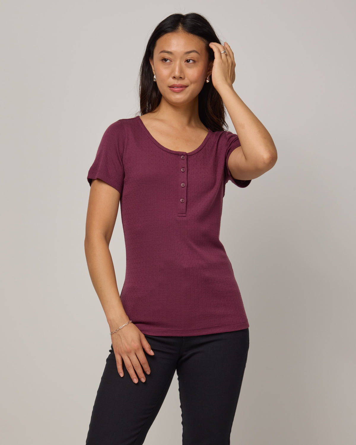 Model wearing Marie Pointelle Henley in Plum, a reddish purple color. Marie Pointelle Henley is a short sleeve, scoop neck, fitted top available in sizes XS-3X. 