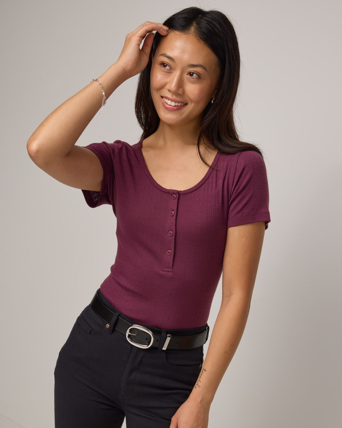 Model wearing Marie Pointelle Henley in Plum, a reddish purple color. Marie Pointelle Henley is a short sleeve, scoop neck, fitted top available in sizes XS-3X. 