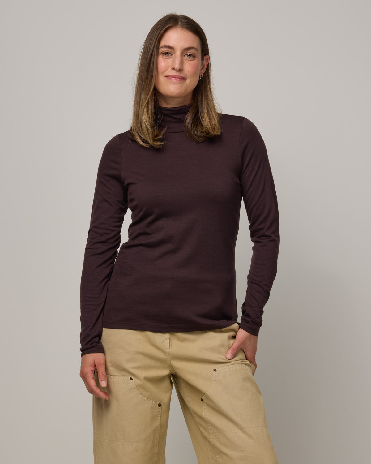 Model wearing Addison Turtleneck Top in Espresso, a dark brown color. Addison Turtleneck Top is a merino wool long sleeve, turtleneck, slim fit top available in sizes XS-3X.