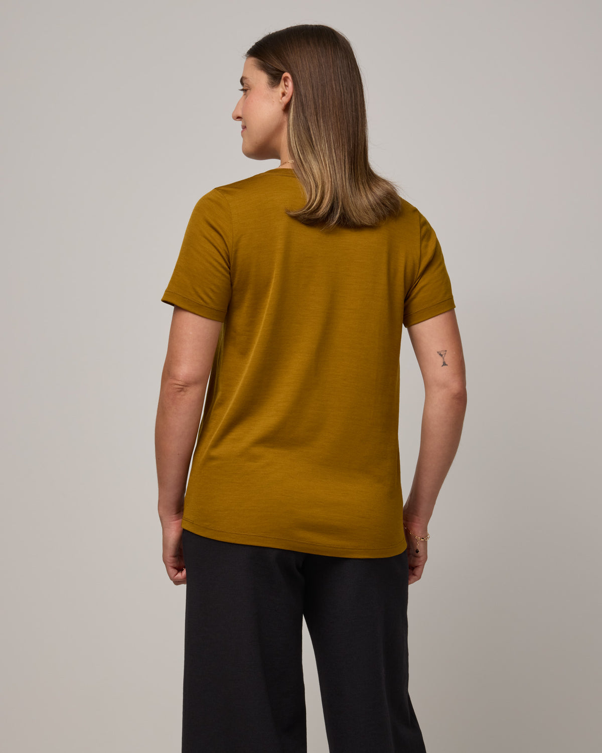 Model wearing Stella Scoop Neck Tee in Spiced Pear, a dark mustard color. Stella Scoop Neck Tee is a merino wool short sleeve, scoop neck t-shirt available in sizes XS-3X.