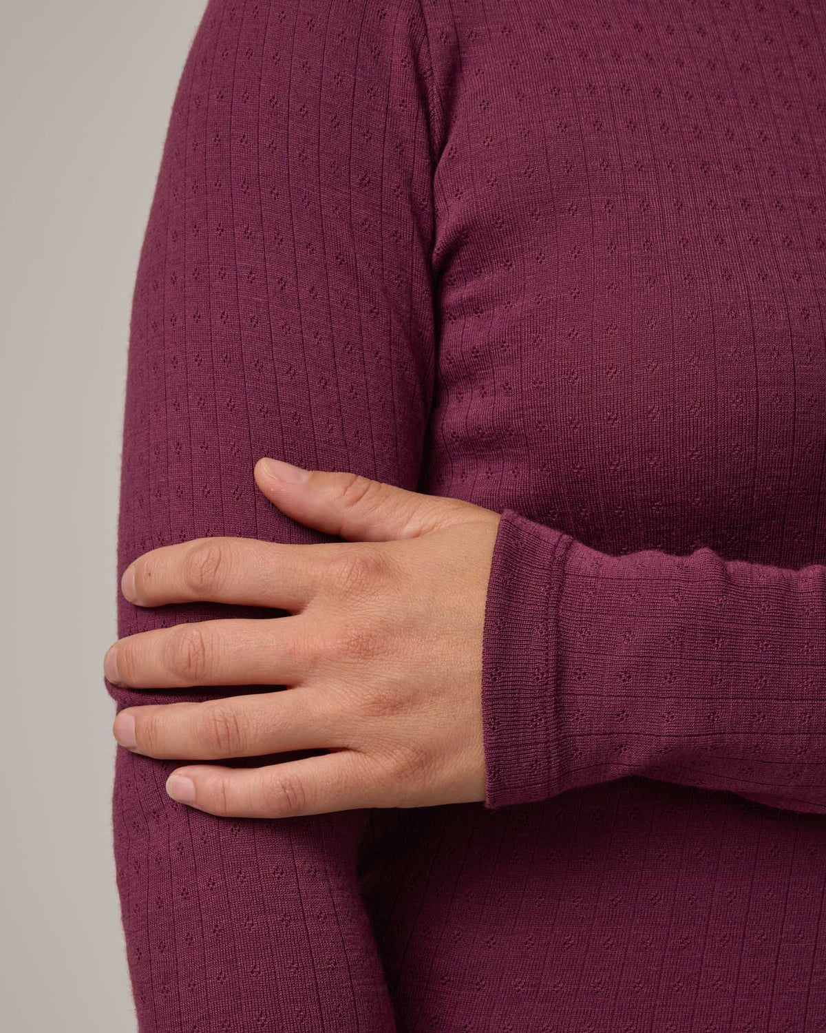 Model wearing Sloan Pointelle Fitted Tee in Plum, a reddish purple color. Sloan Pointelle Fitted Tee is a merino wool long sleeve, crew neck, slim fit tee available in sizes XS-3X.