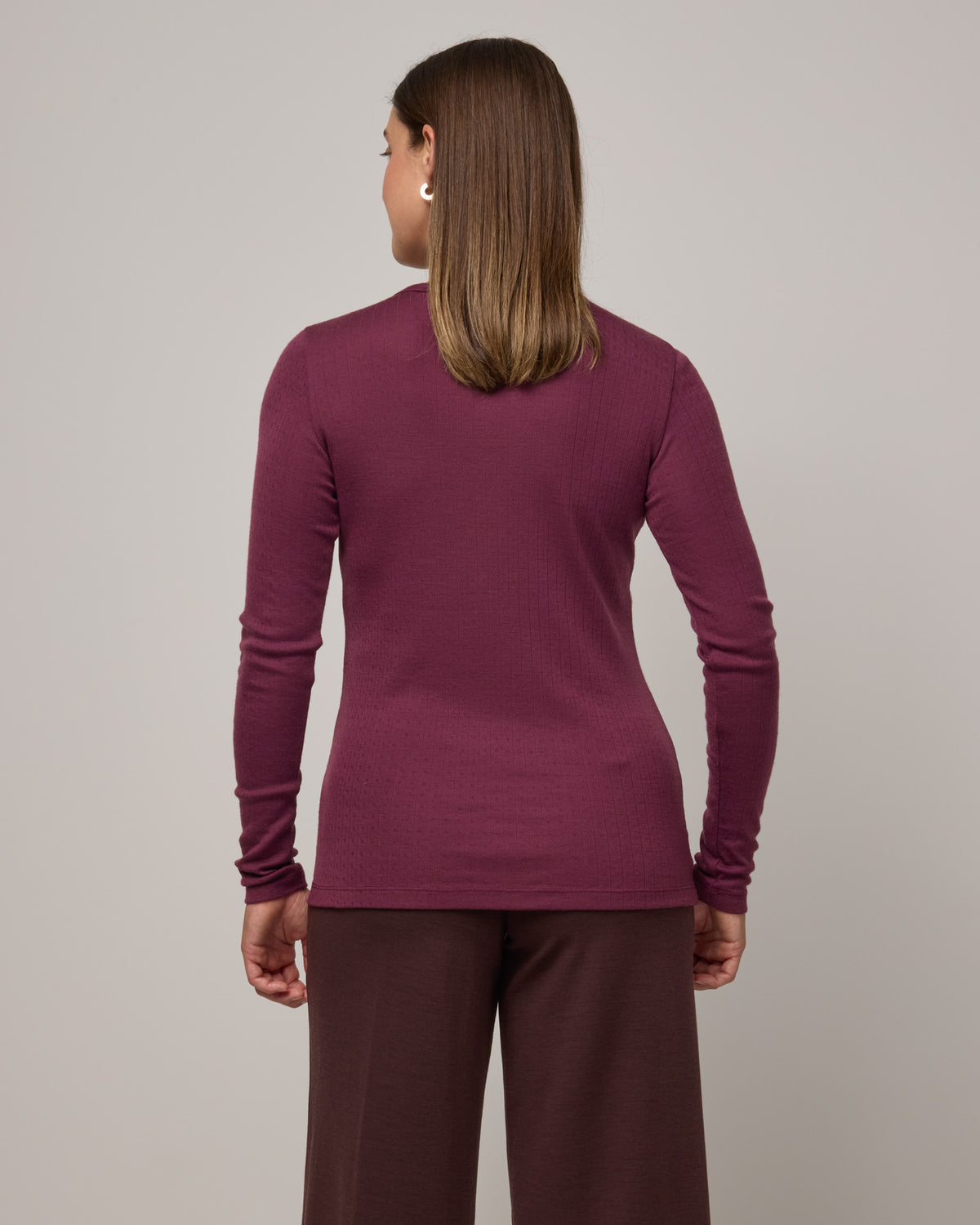 Model wearing Sloan Pointelle Fitted Tee in Plum, a reddish purple color. Sloan Pointelle Fitted Tee is a merino wool long sleeve, crew neck, slim fit tee available in sizes XS-3X.