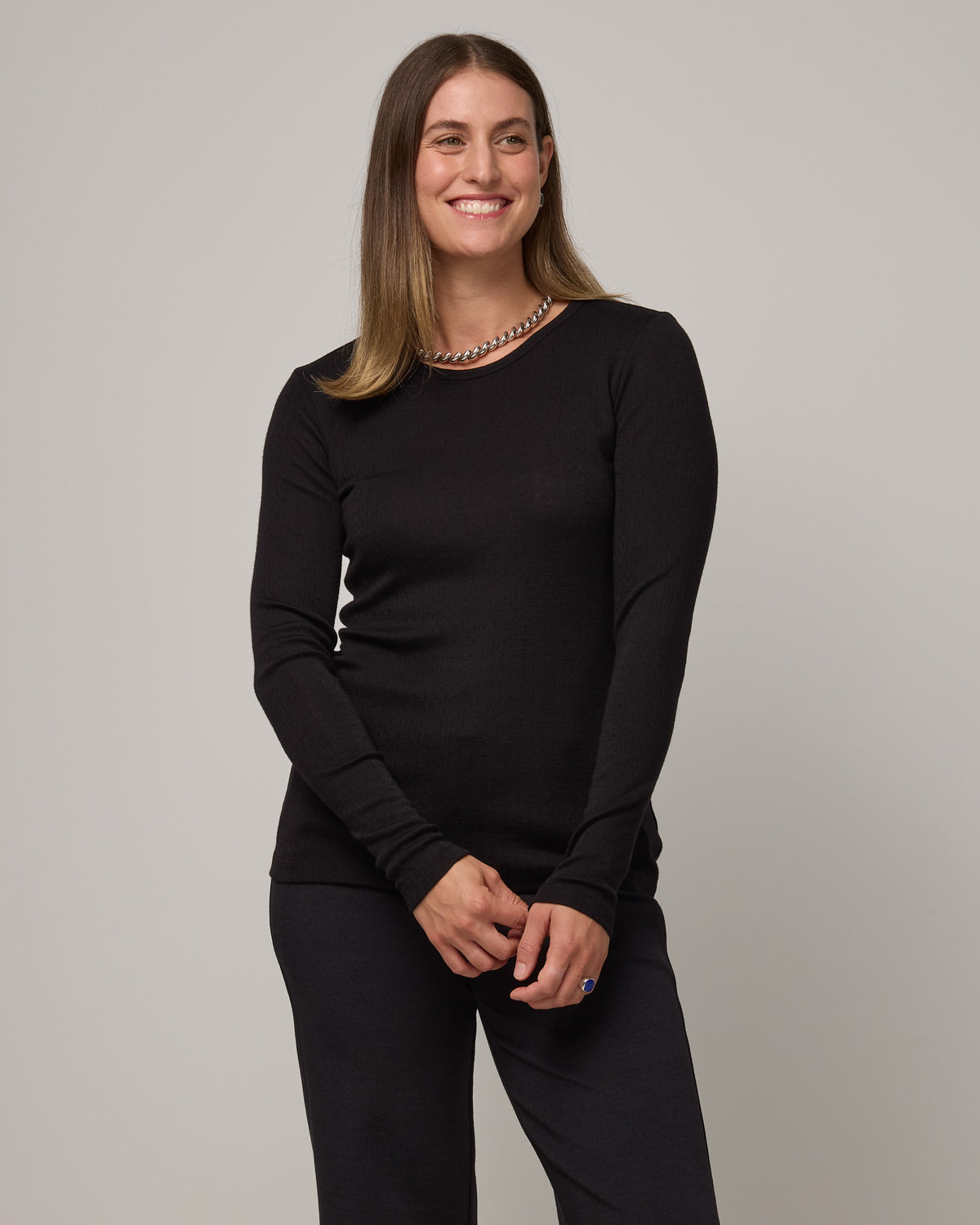 Model wearing Sloan Pointelle Fitted Tee in Black. Sloan Pointelle Fitted Tee is a merino wool long sleeve, crew neck, slim fit tee available in sizes XS-3X.