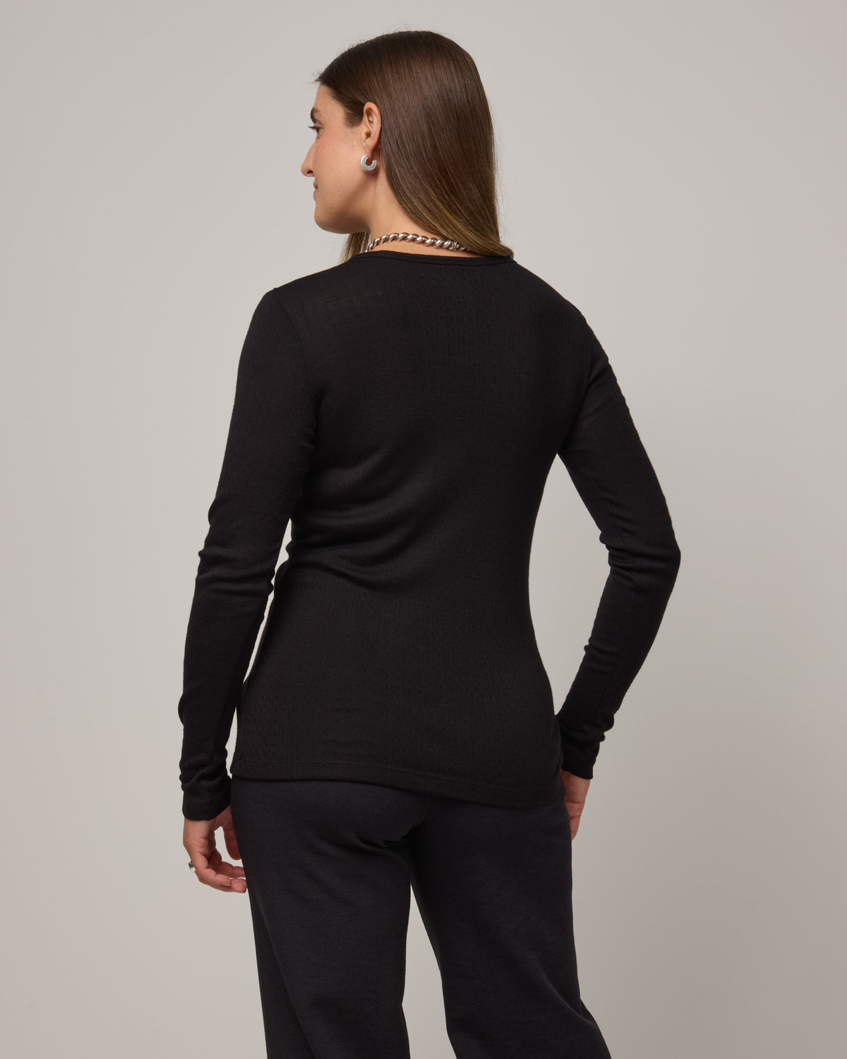 Model wearing Sloan Pointelle Fitted Tee in Black. Sloan Pointelle Fitted Tee is a merino wool long sleeve, crew neck, slim fit tee available in sizes XS-3X.