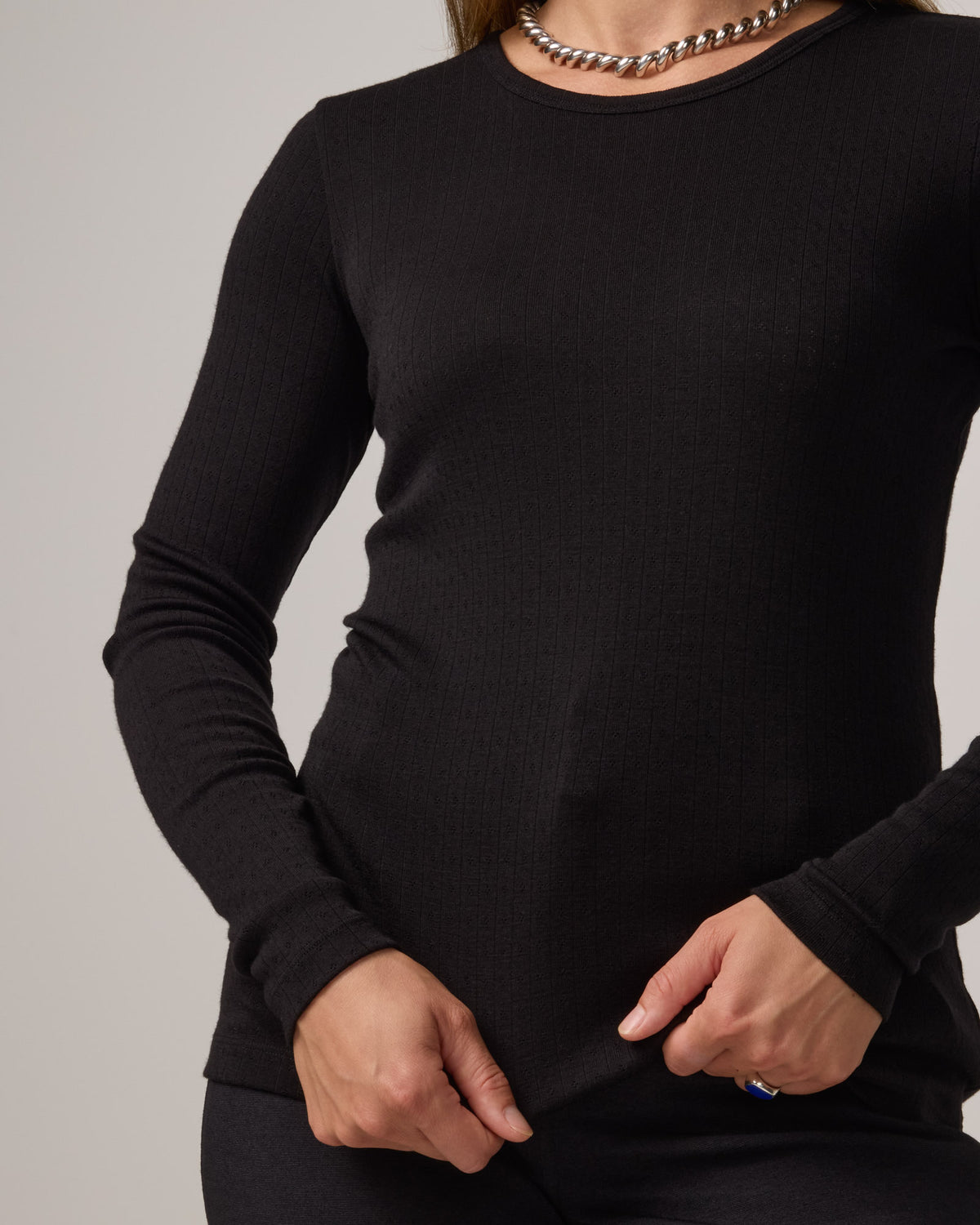 Model wearing Sloan Pointelle Fitted Tee in Black. Sloan Pointelle Fitted Tee is a merino wool long sleeve, crew neck, slim fit tee available in sizes XS-3X.