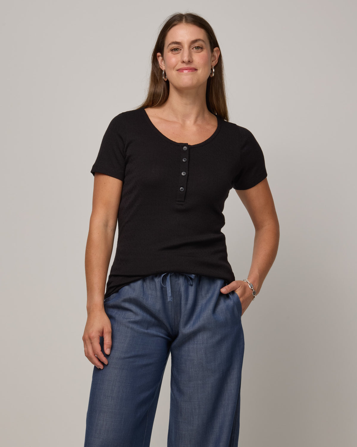 Model wearing Marie Pointelle Henley in Black. Marie Pointelle Henley is a short sleeve, scoop neck, fitted top available in sizes XS-3X. 