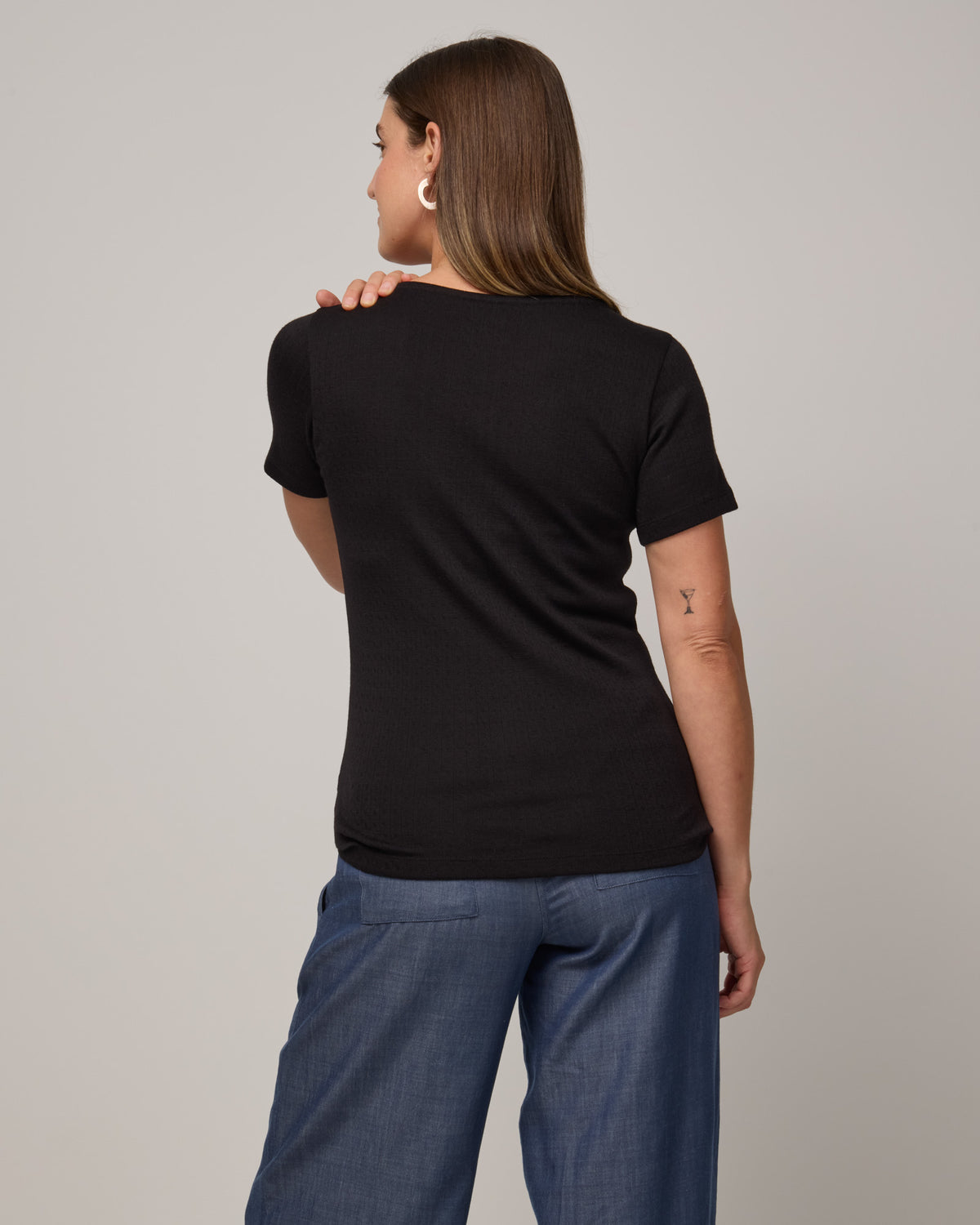 Model wearing Marie Pointelle Henley in Black. Marie Pointelle Henley is a short sleeve, scoop neck, fitted top available in sizes XS-3X. 