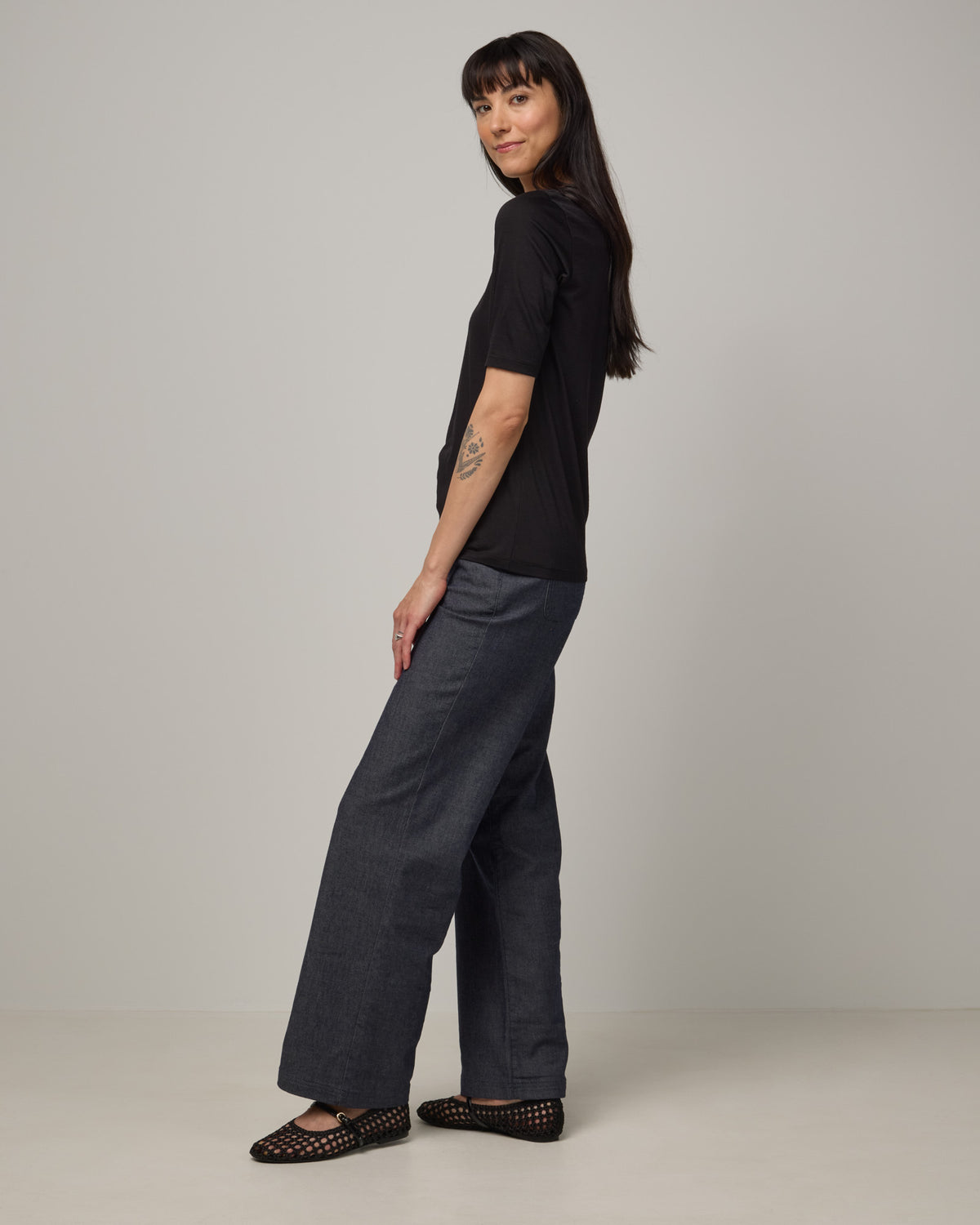 Model wearing Celine Signature Elbow Sleeve Tee in Black. Celine Signature Elbow Sleeve Tee is a merino wool scoop neck tee available in sizes XS-3X.