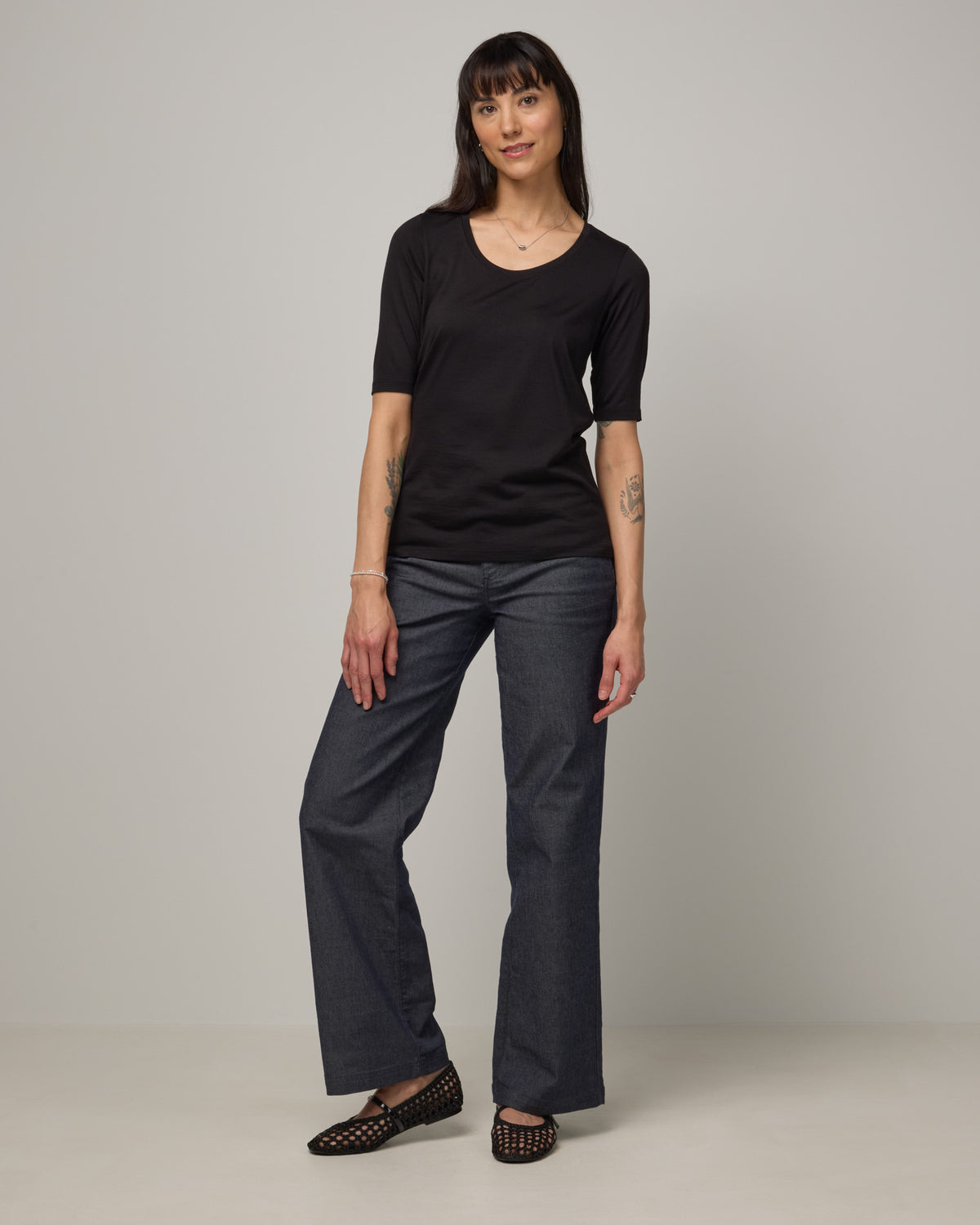 Model wearing Celine Signature Elbow Sleeve Tee in Black. Celine Signature Elbow Sleeve Tee is a merino wool scoop neck tee available in sizes XS-3X.