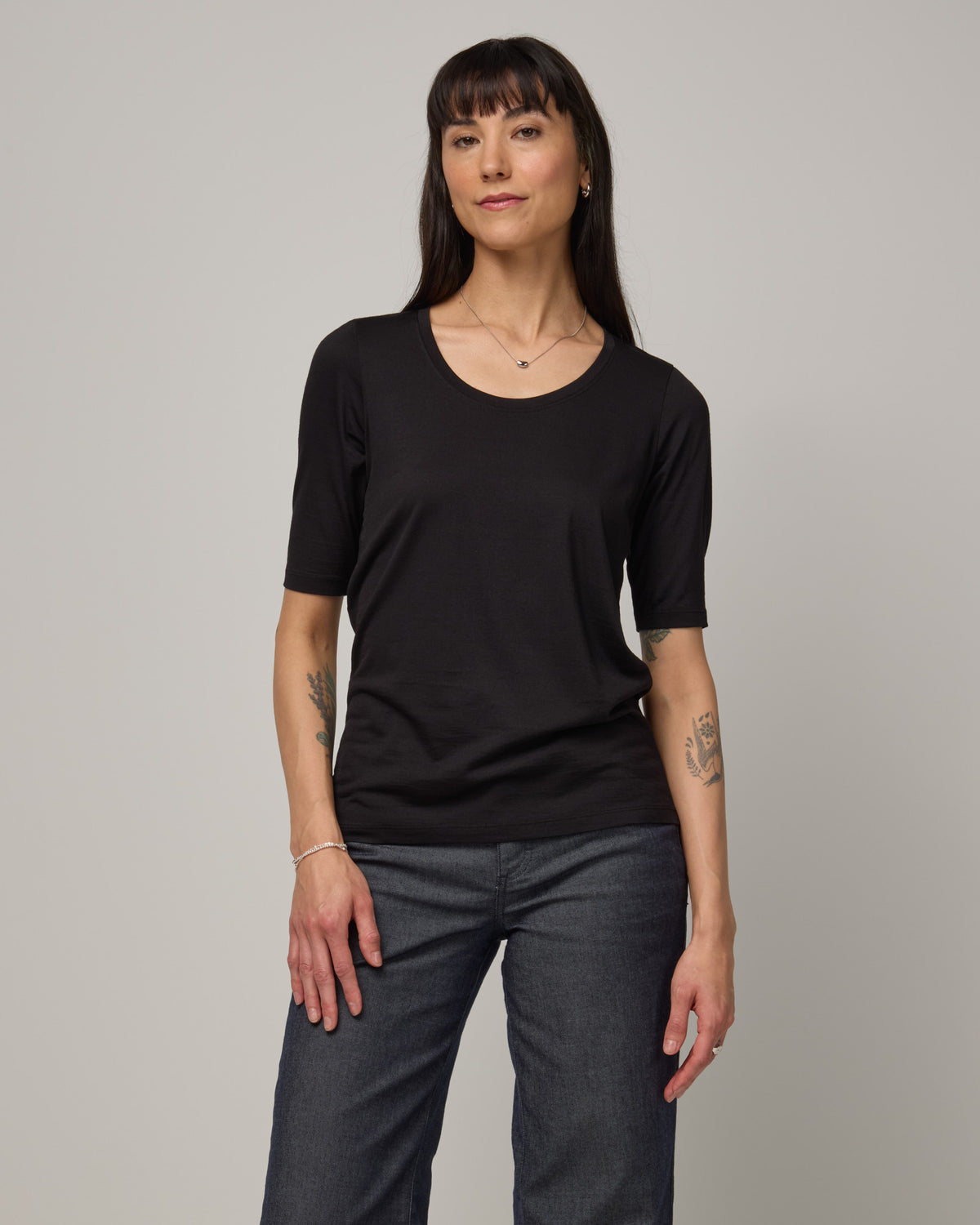 Model wearing Celine Signature Elbow Sleeve Tee in Black. Celine Signature Elbow Sleeve Tee is a merino wool scoop neck tee available in sizes XS-3X.