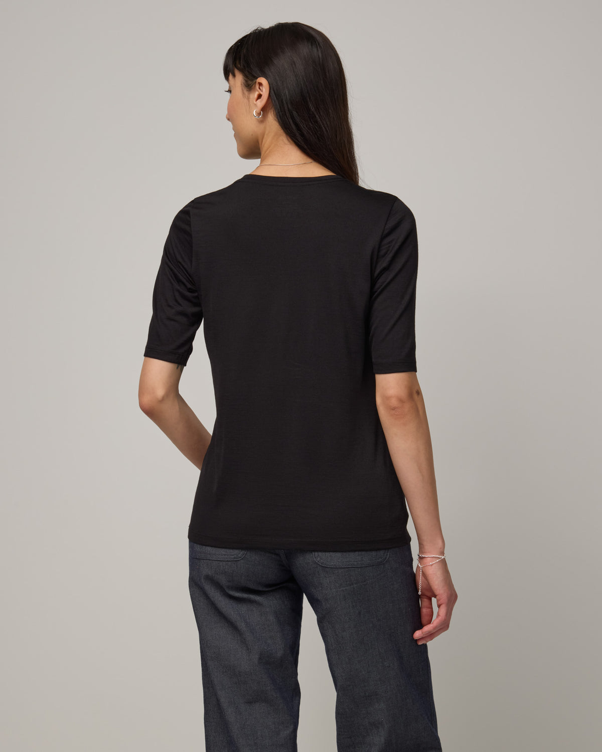 Model wearing Celine Signature Elbow Sleeve Tee in Black. Celine Signature Elbow Sleeve Tee is a merino wool scoop neck tee available in sizes XS-3X.