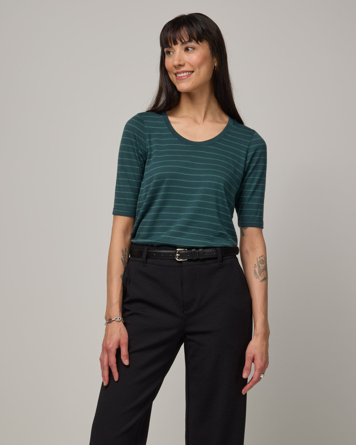 Model wearing Celine Signature Elbow-Sleeve Tee in Pine & Emerald Stripe, a dark green stripe. Celine Signature Elbow Sleeve Tee is a merino wool scoop neck half-sleeve tee available in sizes XS-3X.