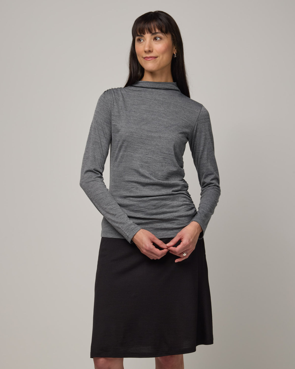 Model wearing Katrina Ruched Top in Charcoal Heather, a heathered dark gray color. Katrina Ruched Top is a long sleeve fitted merino wool mock-turtleneck top available in sizes XS-XXL.
