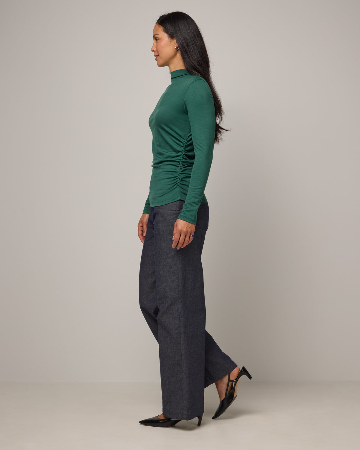 Model wearing Katrina Ruched Top in Emerald green. Katrina Ruched Top is a long sleeve, fitted merino wool mock turtleneck top available in sizes XS-XXL.