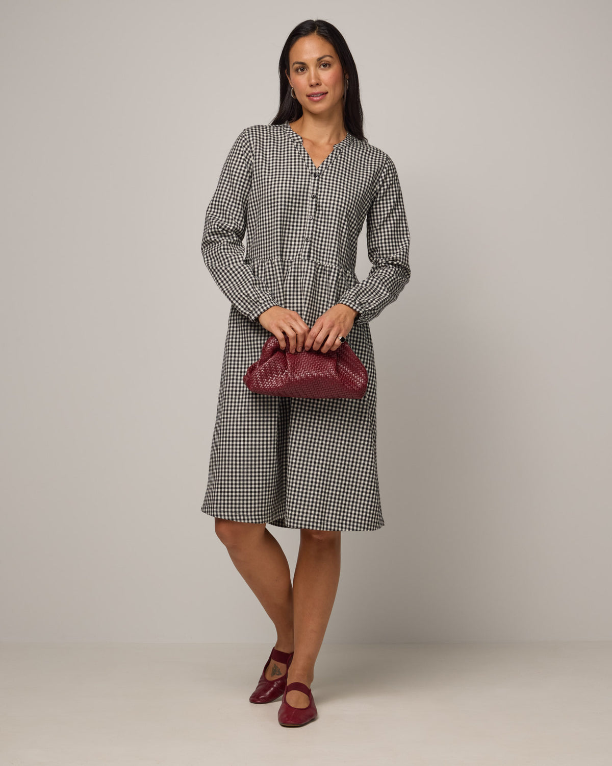 Model wearing Marika Brushed Twill Dress in Black & White Gingham. Marika Brushed Twill Dress is a merino wool long sleeve, gathered, midi swing dress with a button placket available in sizes XS-XXL.