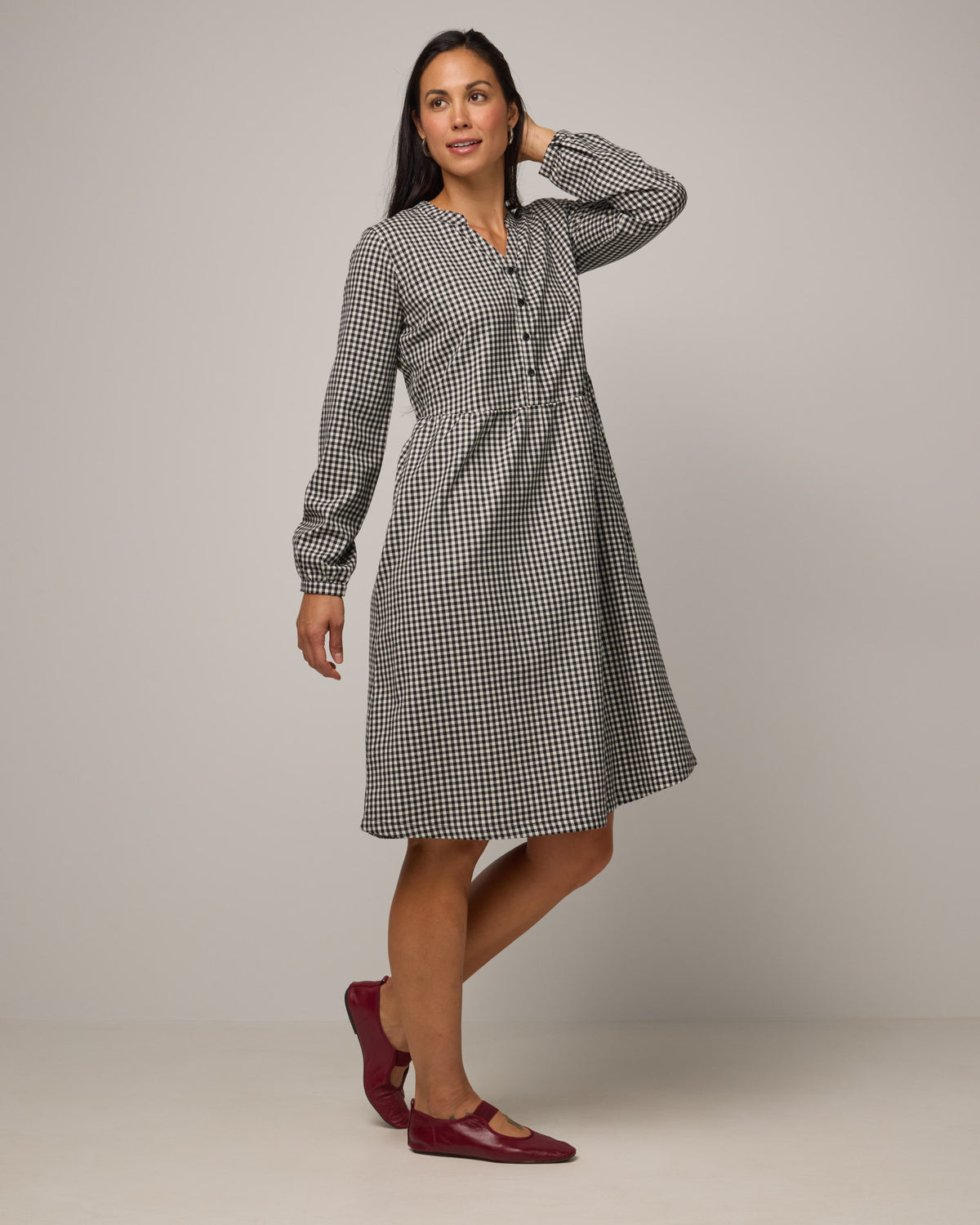 Model wearing Marika Brushed Twill Dress in Black & White Gingham. Marika Brushed Twill Dress is a merino wool long sleeve, gathered, midi swing dress with a button placket available in sizes XS-XXL.