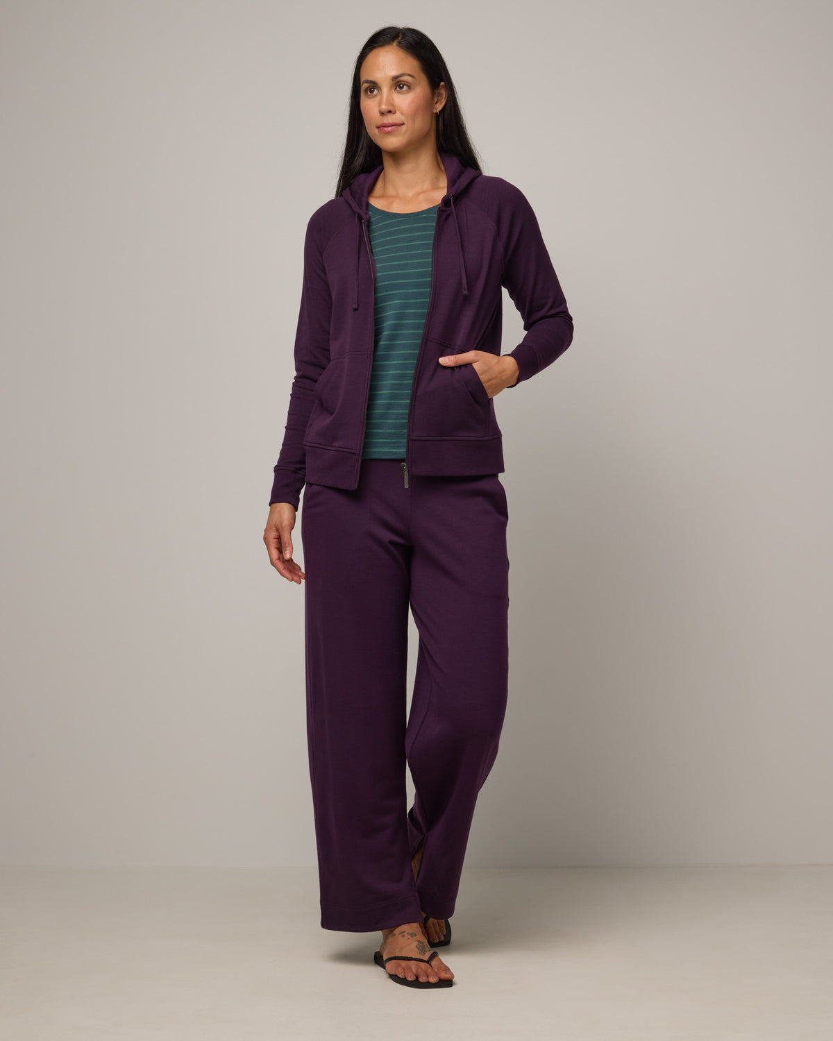 Model wearing Aspen Full-Zip Hoodie in Cassis, a deep purple color. Aspen Full-Zip Hoodie is a merino wool long sleeve zip hoodie with pockets available in sizes XS-3X.
