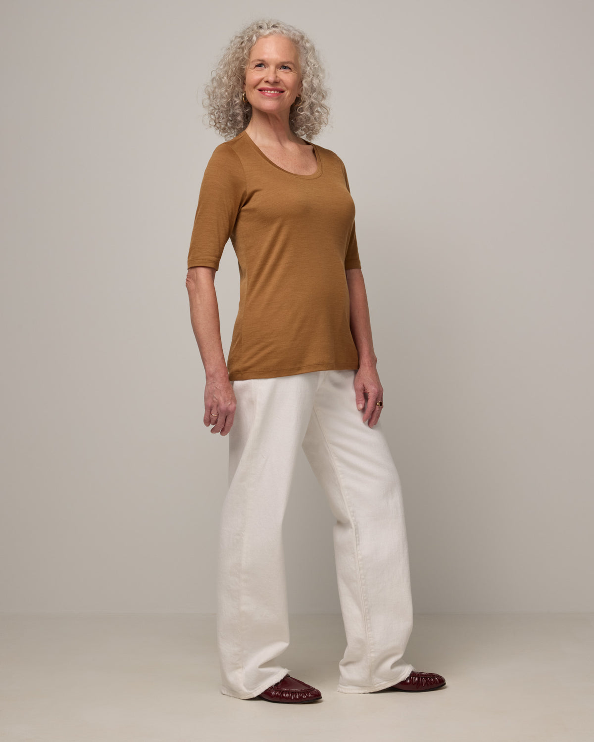 Model wearing Celine Signature Elbow-Sleeve Tee in Camel, a caramel brown color. Celine Signature Elbow Sleeve Tee is a merino wool scoop neck half-sleeve tee available in sizes XS-3X.