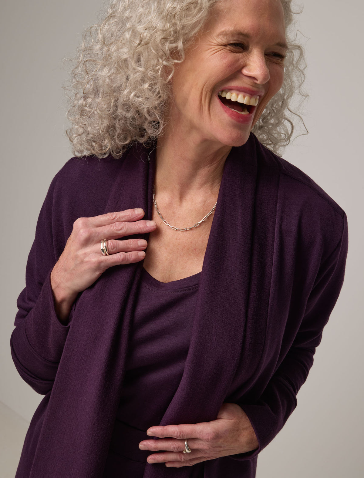 Model wearing Aspen Cardigan in Cassis, a dark purple color. Aspen Cardigan is a merino wool long sleeve cardigan with pockets available in sizes XS-3X.