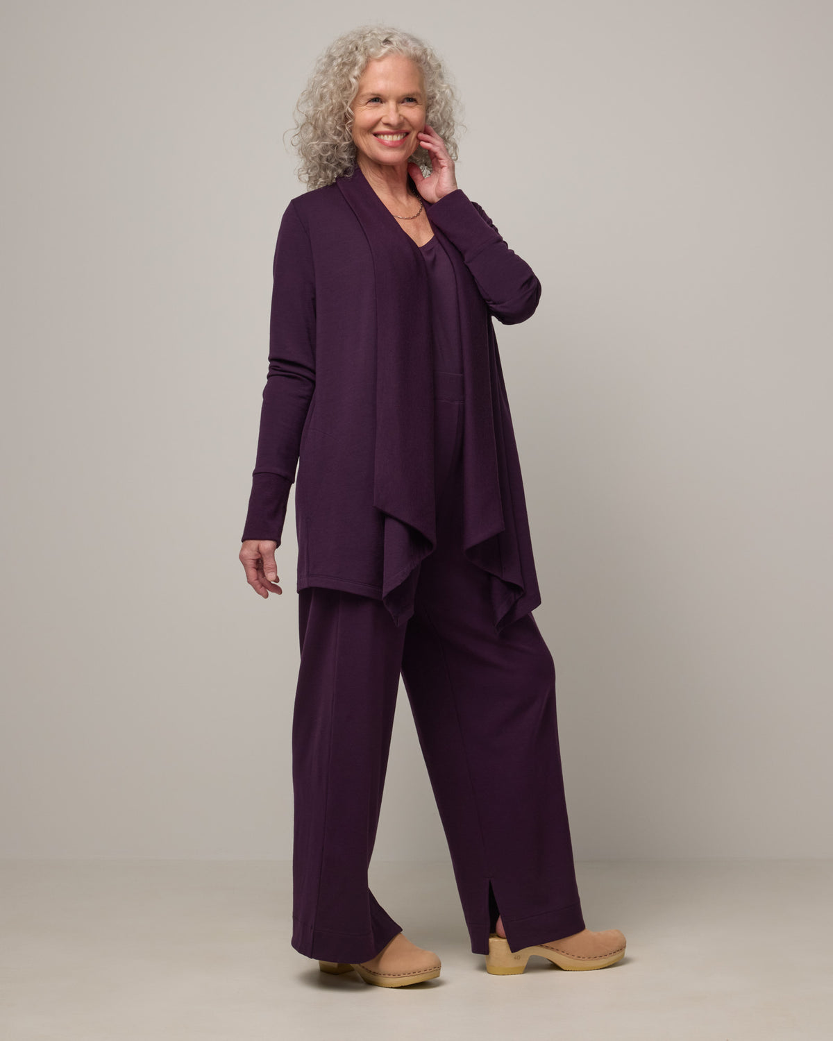 Model wearing Aspen Cardigan in Cassis, a dark purple color. Aspen Cardigan is a merino wool long sleeve cardigan with pockets available in sizes XS-3X.