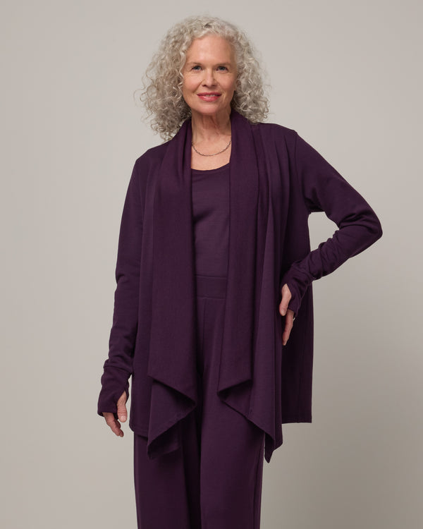 Model wearing Aspen Cardigan in Cassis, a dark purple color. Aspen Cardigan is a merino wool long sleeve cardigan with pockets available in sizes XS-3X.