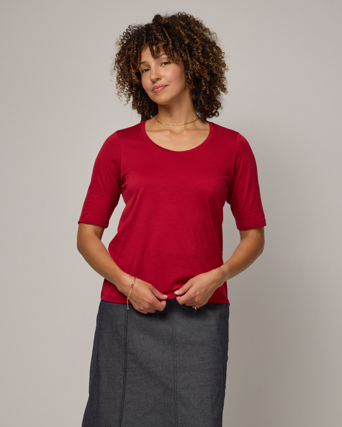 Model wearing Celine Signature Elbow-Sleeve Tee in Cherry Red, a bright red color. Celine Signature Elbow Sleeve Tee is a merino wool scoop neck half-sleeve tee available in sizes XS-3X. 