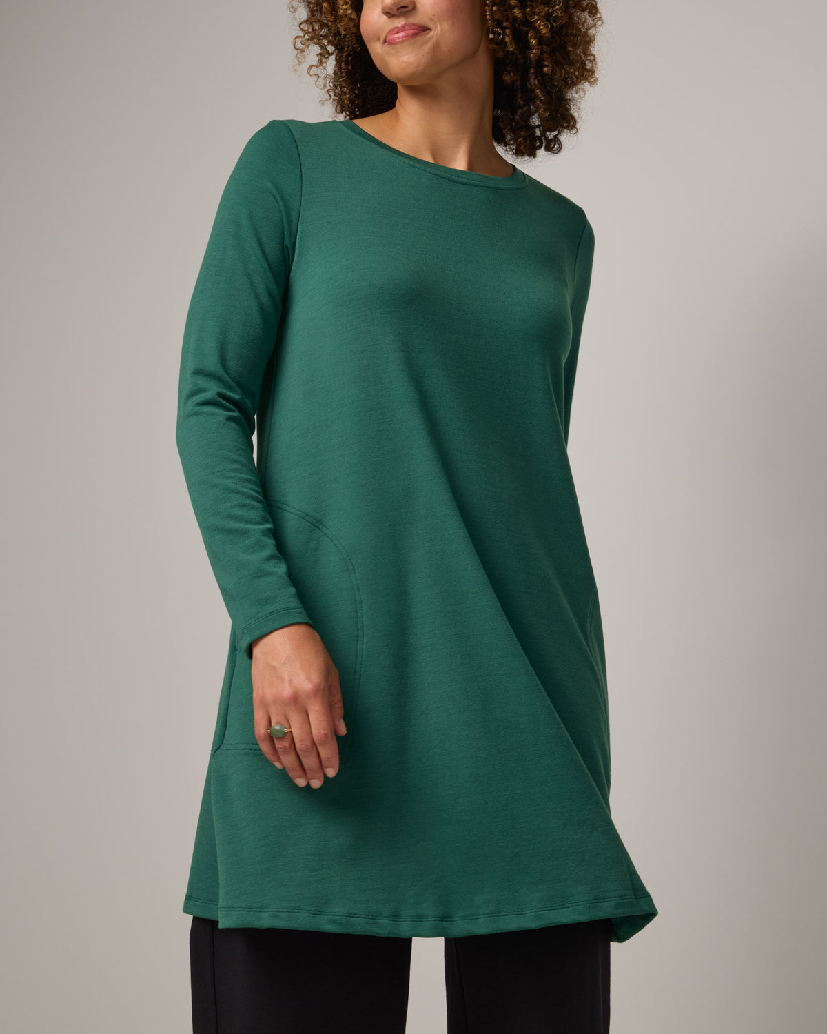 Model wearing Eliza Swing Dress in Emerald green. Eliza Swing Dress is a merino wool long sleeve, crew neck, knee length swing dress with pockets available in sizes XS-3X Regular, XS-3X Long.