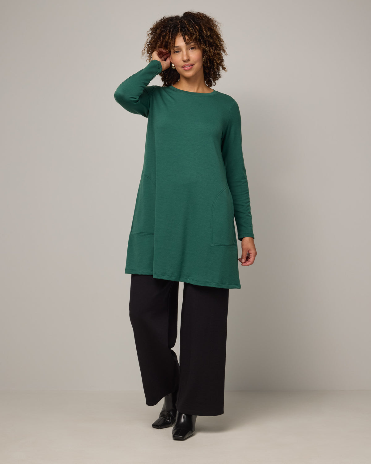 Model wearing Eliza Swing Dress in Emerald green. Eliza Swing Dress is a merino wool long sleeve, crew neck, knee length swing dress with pockets available in sizes XS-3X Regular, XS-3X Long.